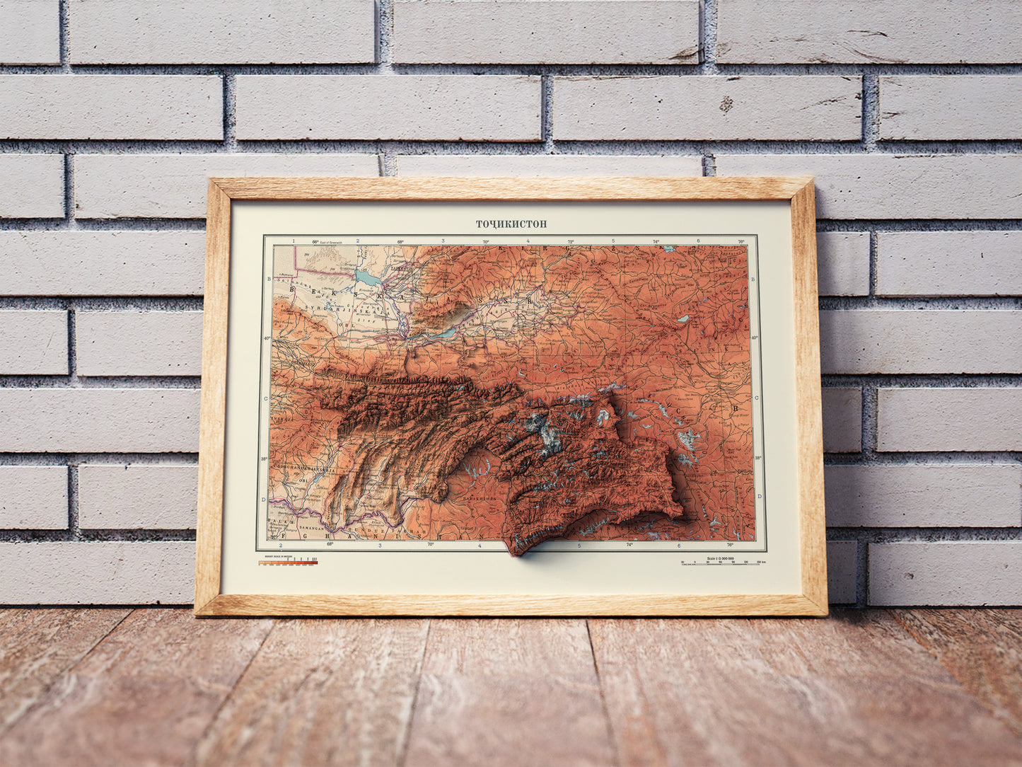 Vintage Tajikistan shaded relief map in a wooden frame. Realistic terrain art print for home decor, displayed against a brick wall