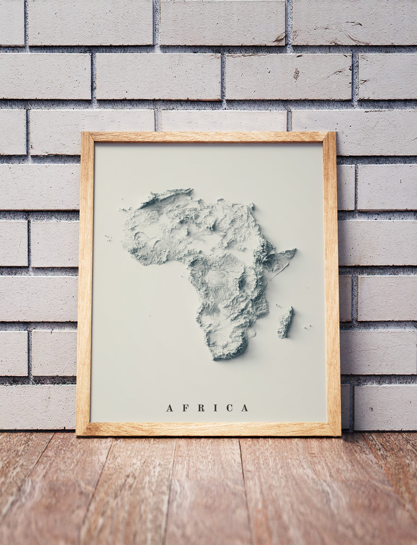 Africa shaded relief map in a wooden frame. Realistic terrain art print for home decor, displayed against a brick wall
