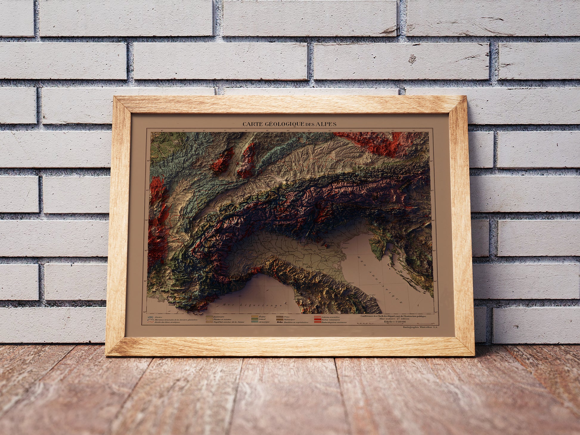 Vintage Alps shaded relief map in a wooden frame. Realistic terrain art print for home decor, displayed against a brick wall