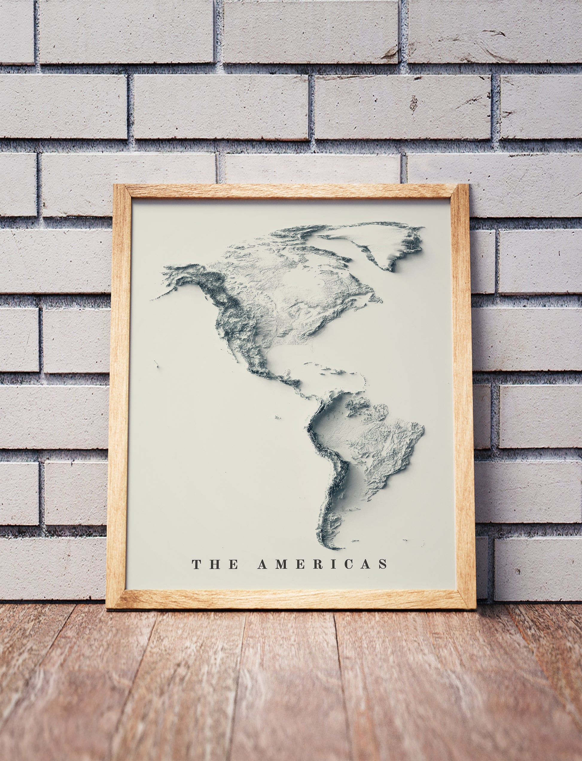 American Continent shaded relief map in a wooden frame. Realistic terrain art print for home decor, displayed against a brick wall
