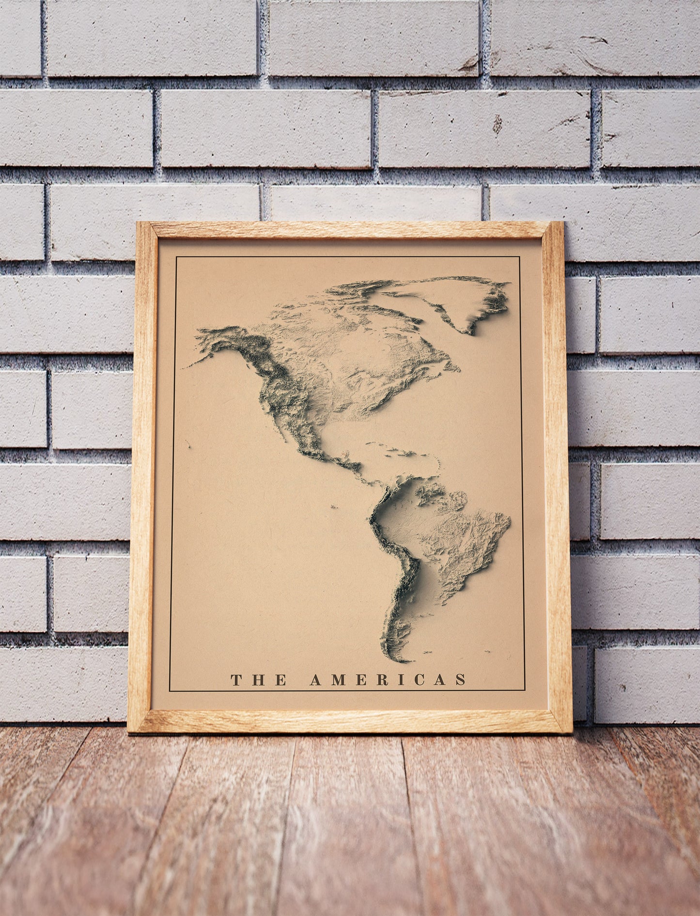Vintage American Continent shaded relief map in a wooden frame. Realistic terrain art print for home decor, displayed against a brick wall