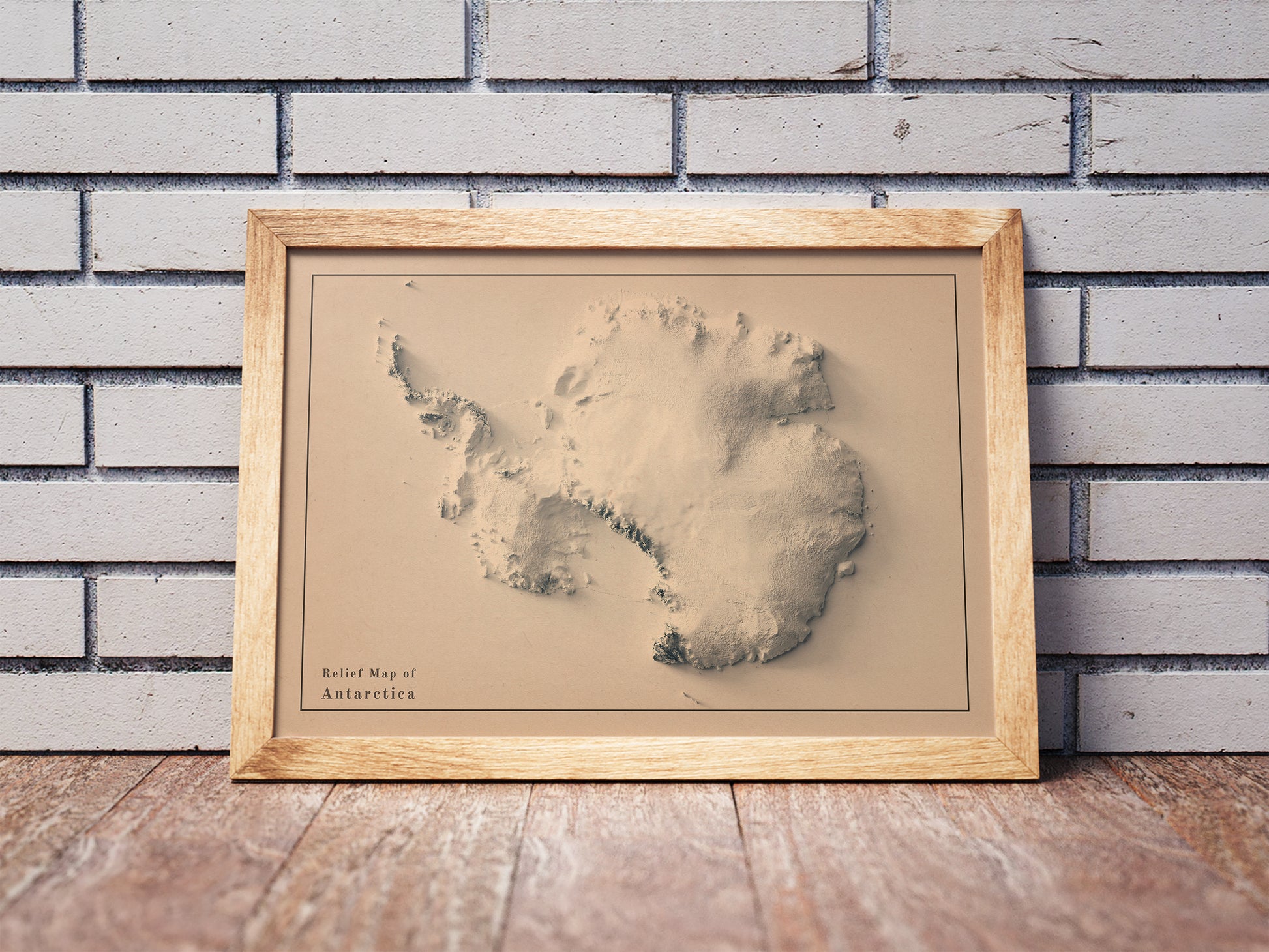Vintage Antarctic shaded relief map in a wooden frame. Realistic terrain art print for home decor, displayed against a brick wall