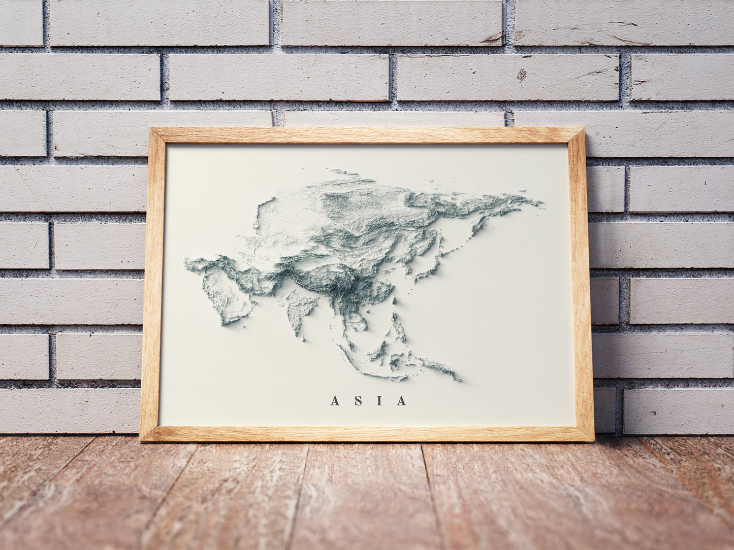 Asia shaded relief map in a wooden frame. Realistic terrain art print for home decor, displayed against a brick wall