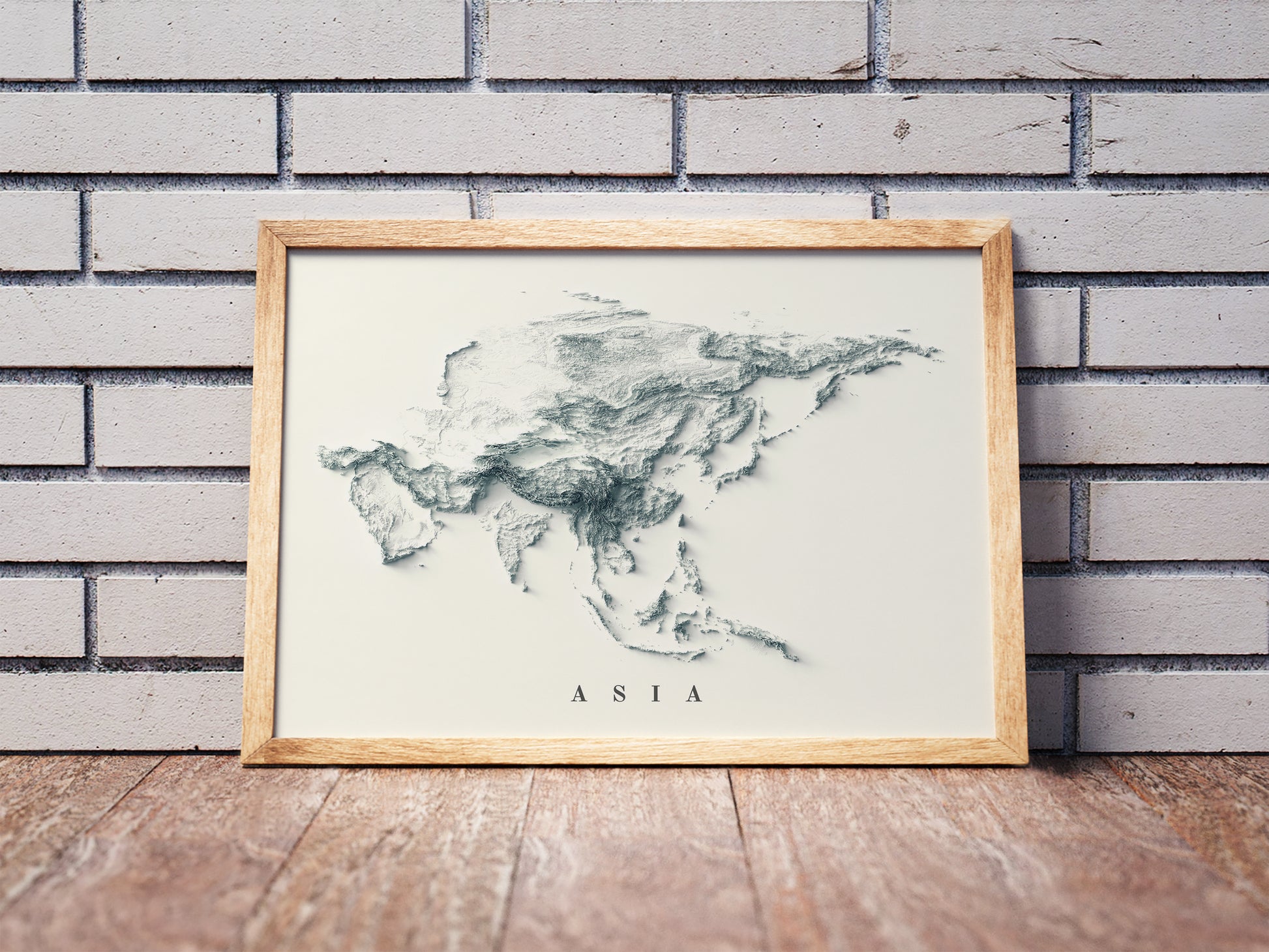 Asia shaded relief map in a wooden frame. Realistic terrain art print for home decor, displayed against a brick wall