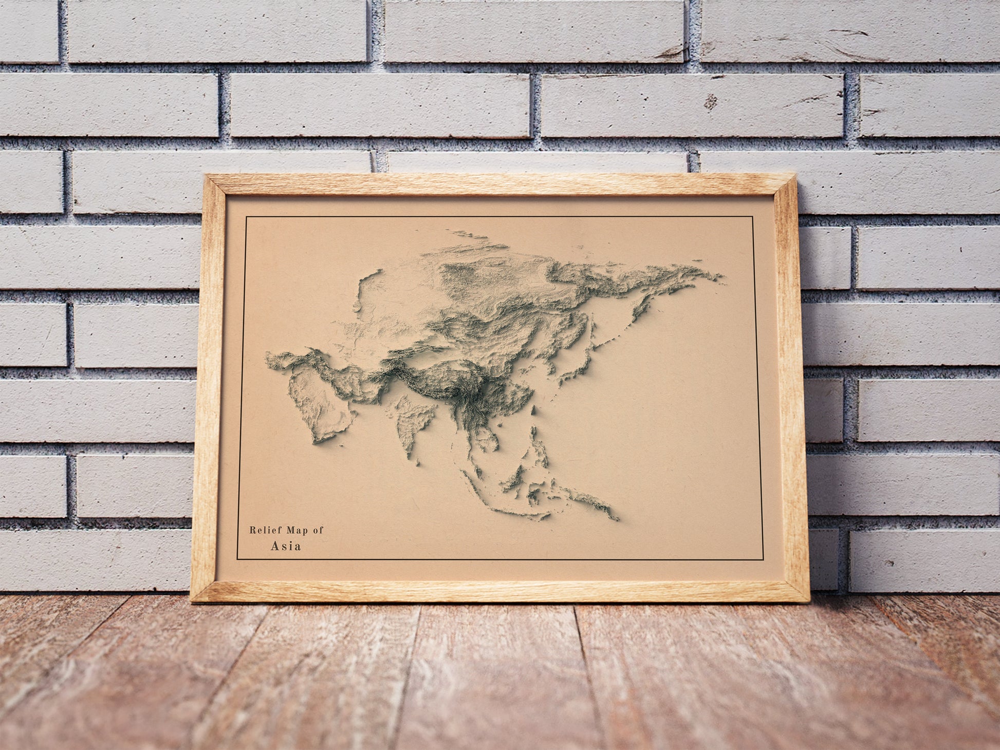 Asia shaded relief map in a wooden frame. Realistic terrain art print for home decor, displayed against a brick wall
