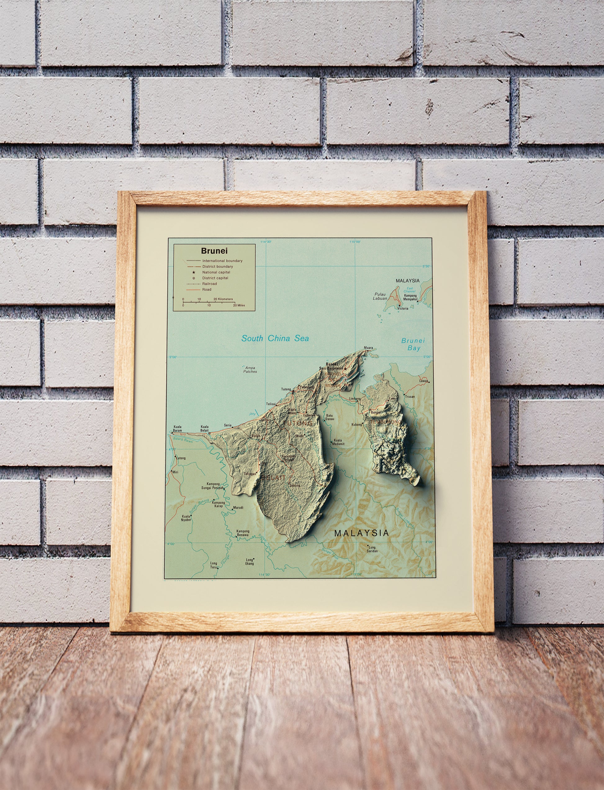 Vintage Brunei shaded relief map in a wooden frame. Realistic terrain art print for home decor, displayed against a brick wall