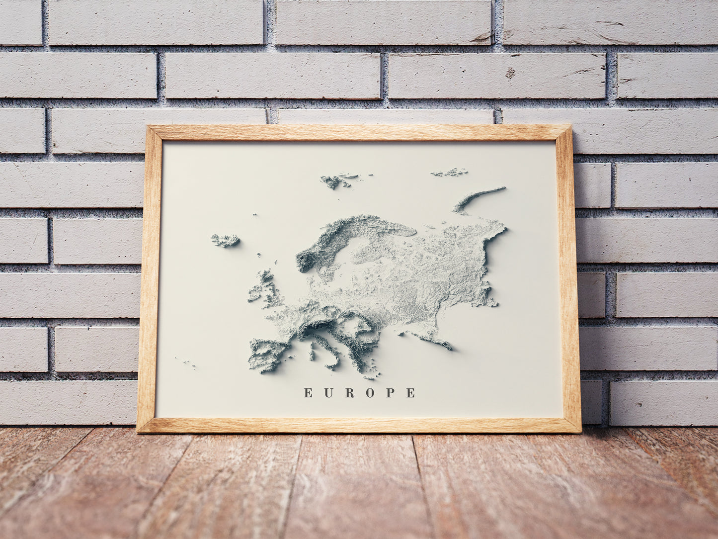 Vintage Europe shaded relief map in a wooden frame. Realistic terrain art print for home decor, displayed against a brick wall