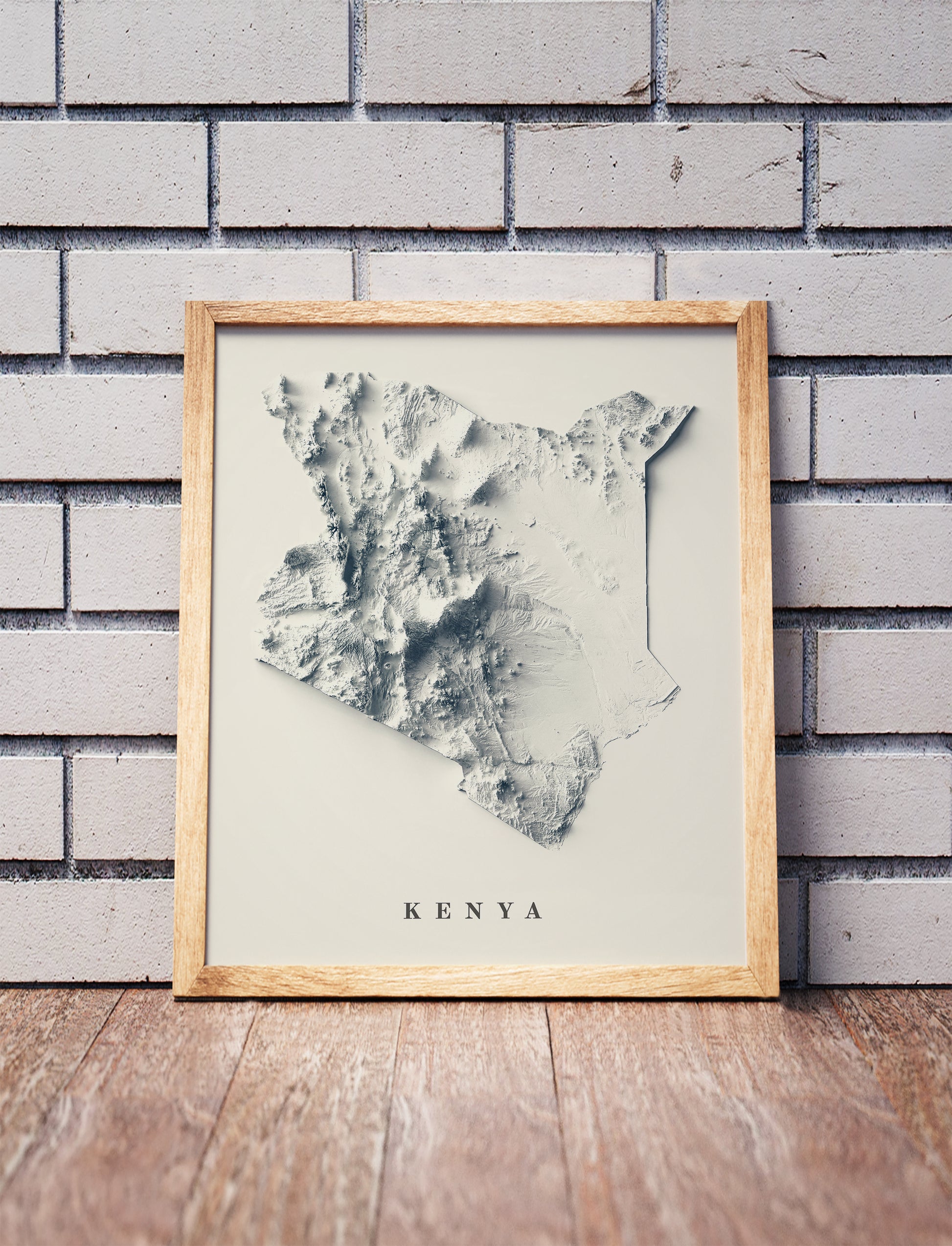 Kenya shaded relief map in a wooden frame. Realistic terrain art print for home decor, displayed against a brick wall