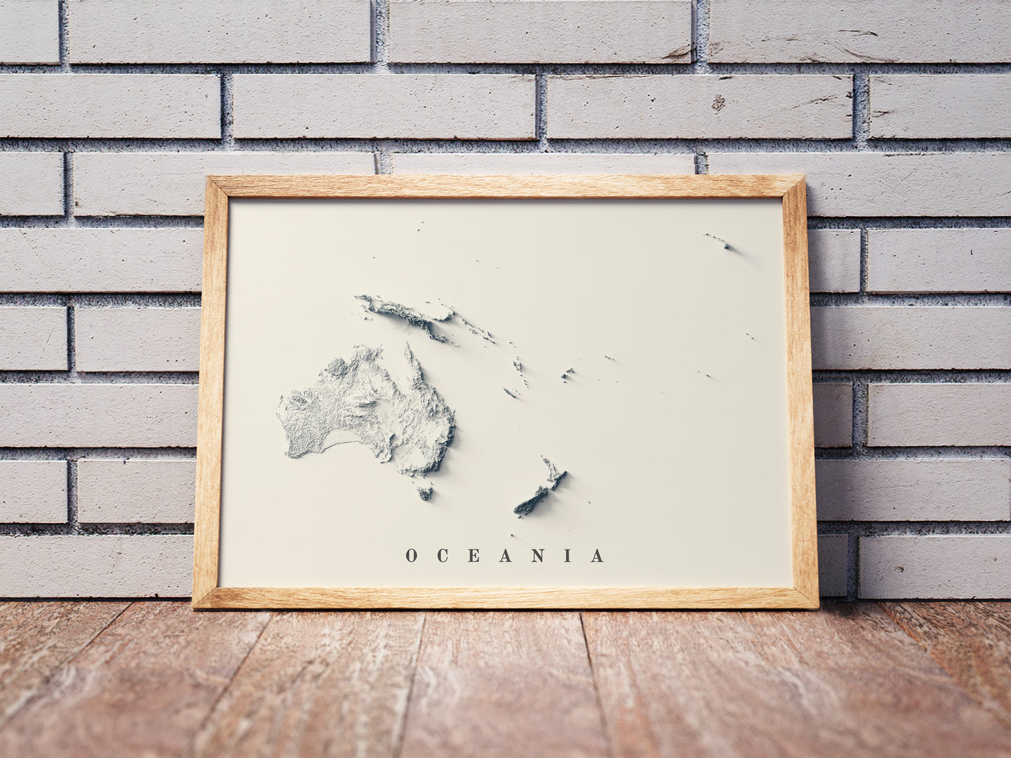 Oceania shaded relief map in a wooden frame. Realistic terrain art print for home decor, displayed against a brick wall