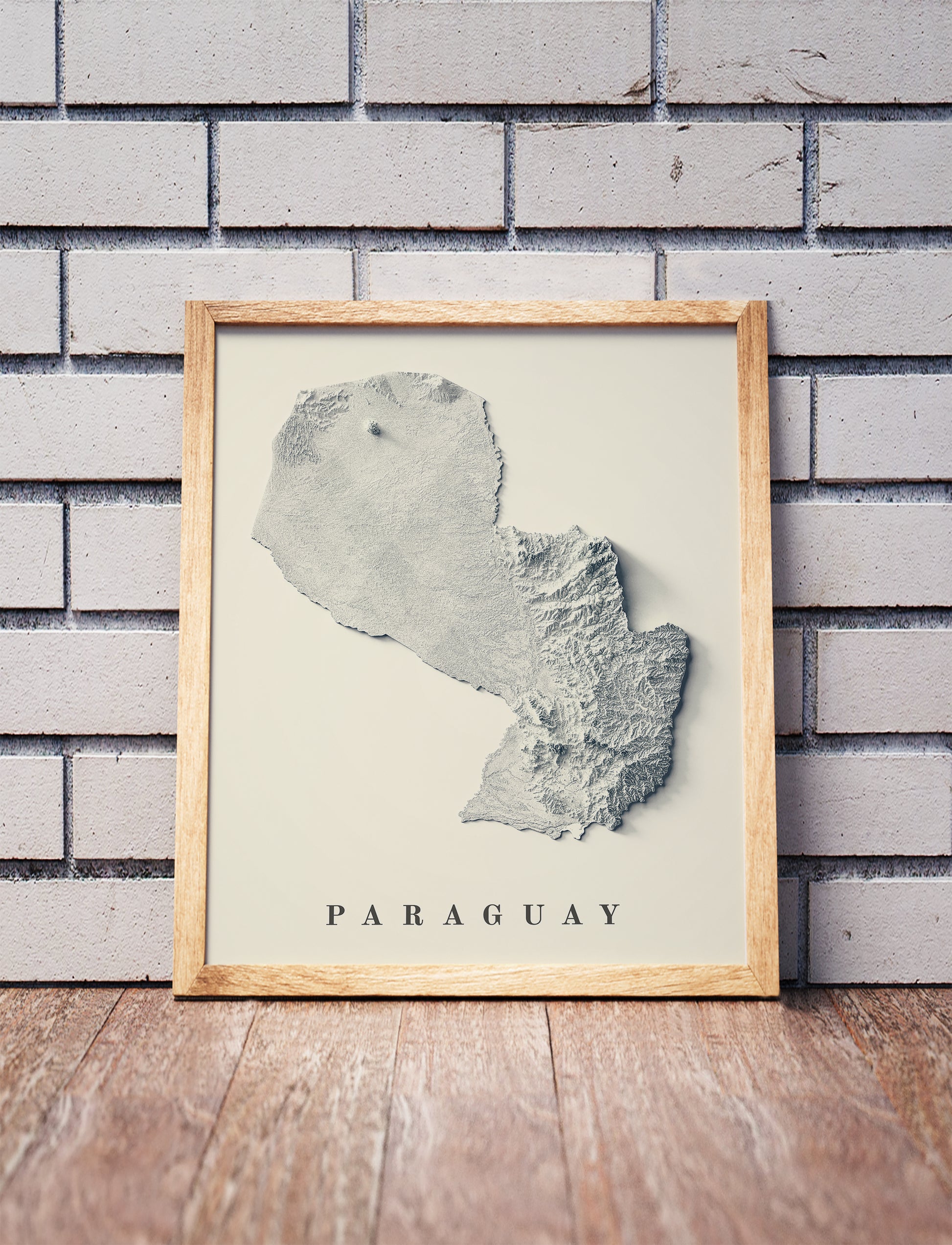 Paraguay shaded relief map in a wooden frame. Realistic terrain art print for home decor, displayed against a brick wall