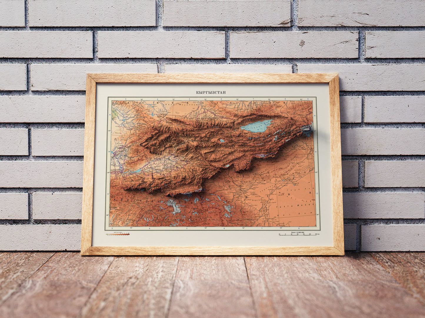 Vintage Kyrgyzstan shaded relief map in a wooden frame. Realistic terrain art print for home decor, displayed against a brick wall