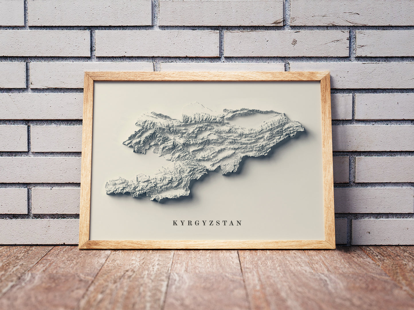 Vintage Kyrgyzstan shaded relief map in a wooden frame. Realistic terrain art print for home decor, displayed against a brick wall