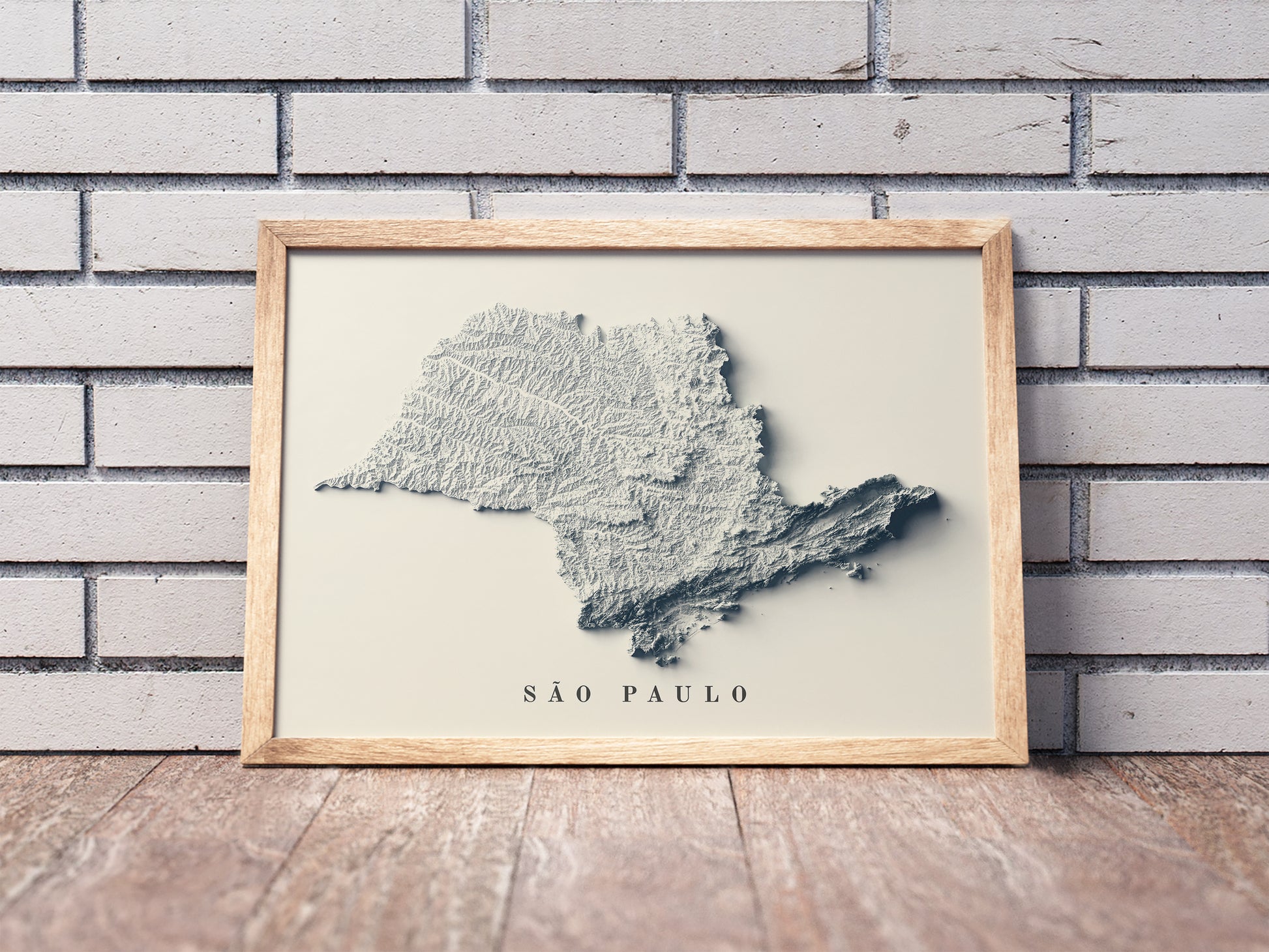 Sao Paulo (Brazil) shaded relief map in a wooden frame. Realistic terrain art print for home decor, displayed against a brick wall