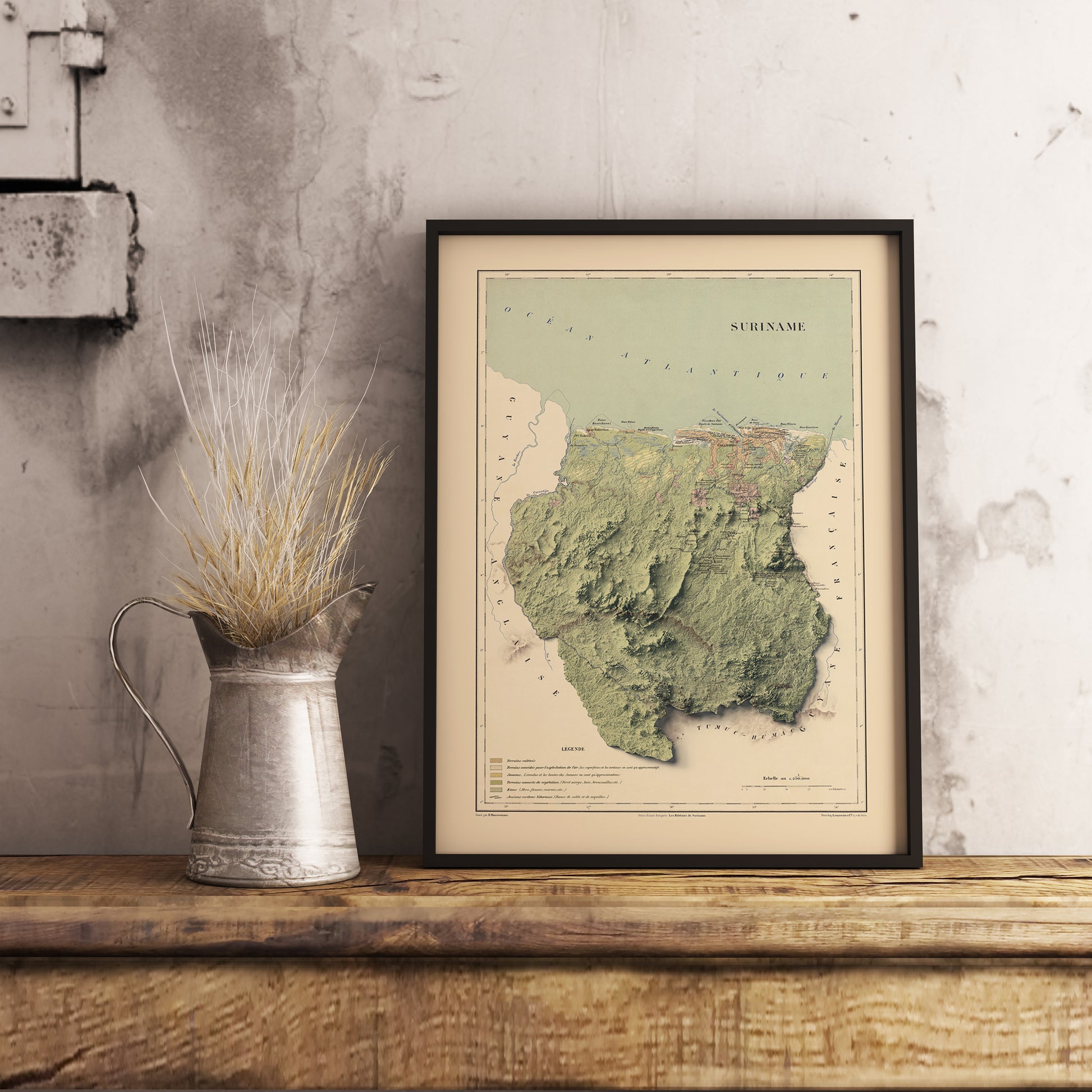 Vintage Suriname shaded relief map in black frame. Realistic terrain art print for home decor, displayed on rustic wooden table