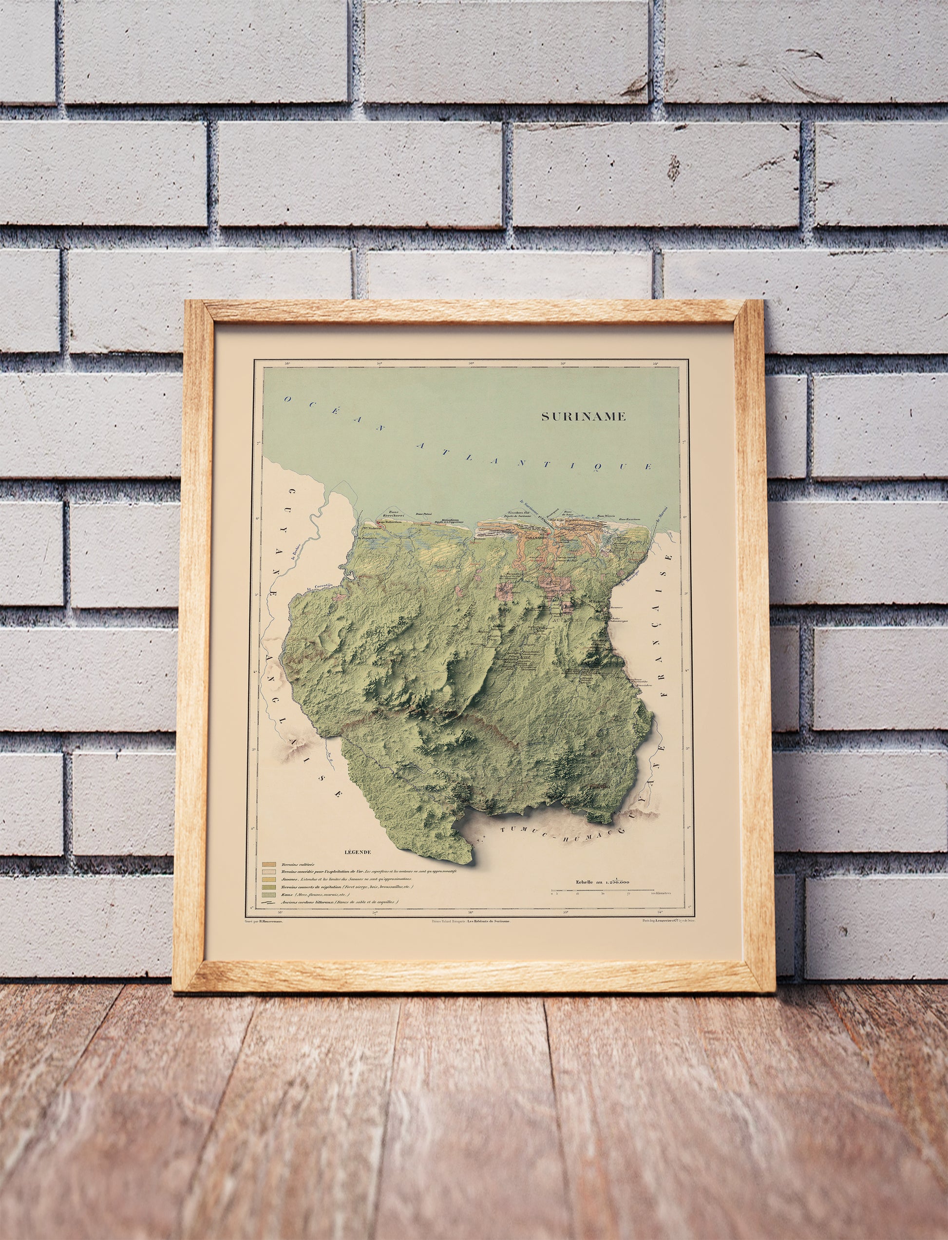 Vintage Suriname shaded relief map in a wooden frame. Realistic terrain art print for home decor, displayed against a brick wall