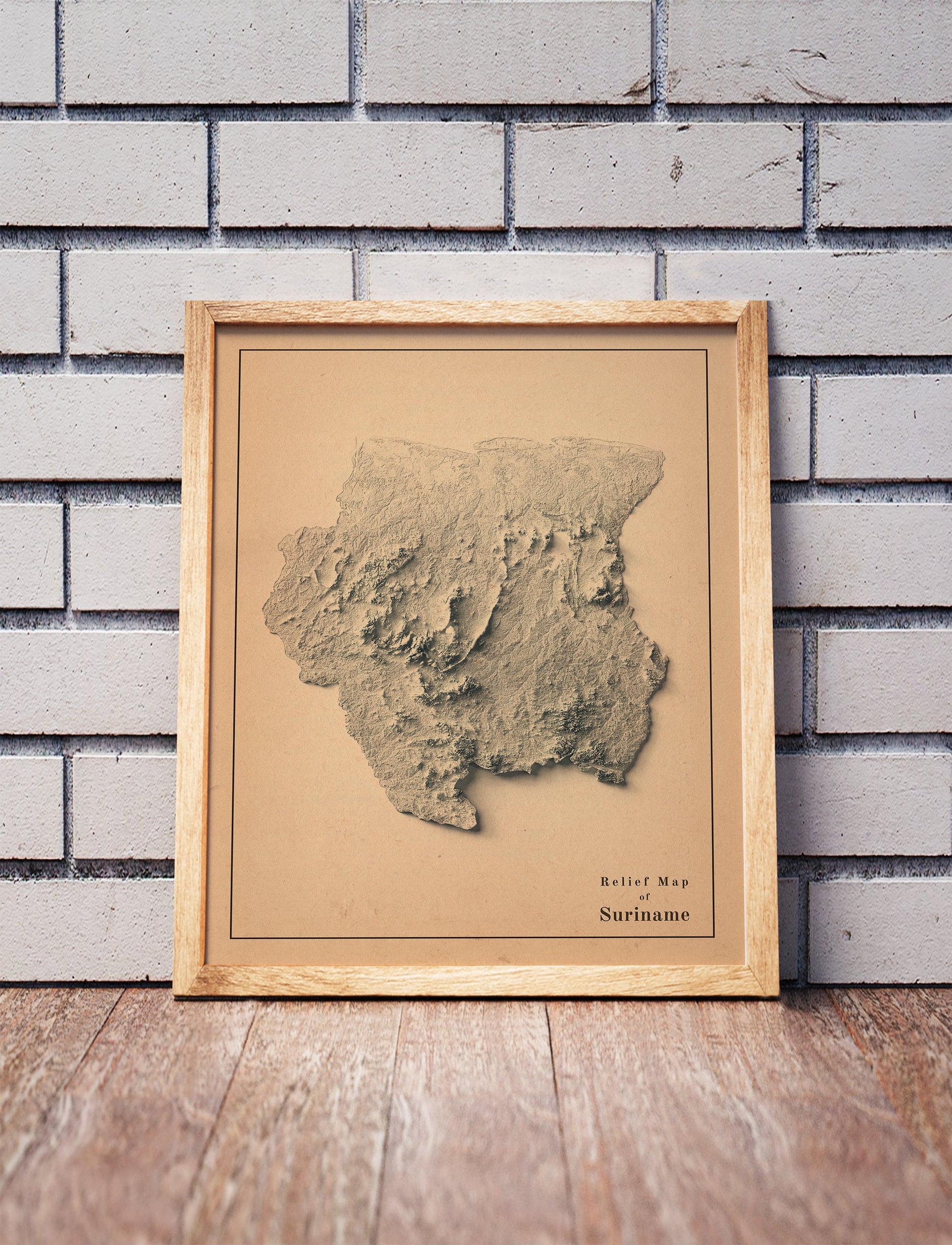 Vintage Suriname shaded relief map in a wooden frame. Realistic terrain art print for home decor, displayed against a brick wall