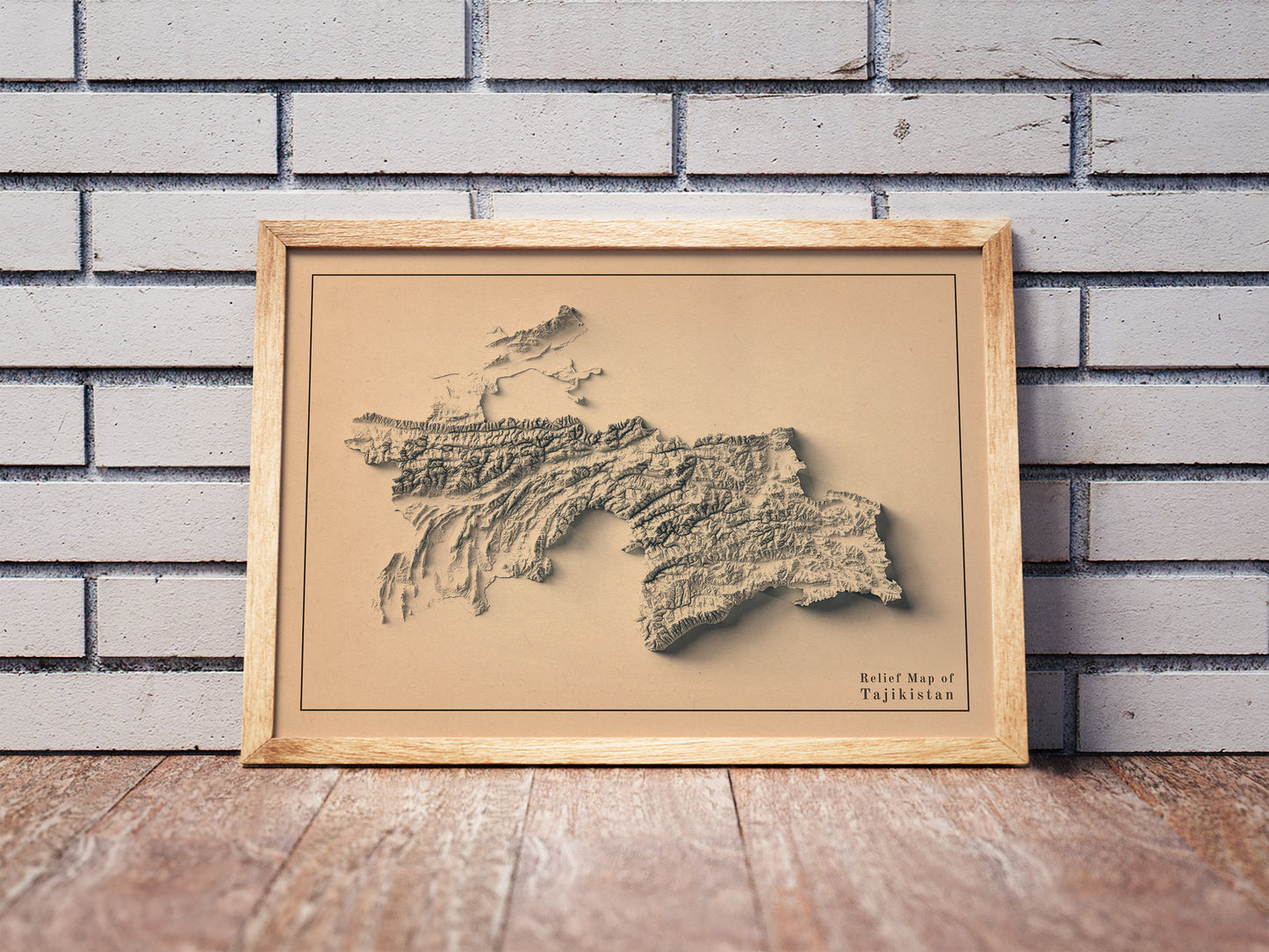 Vintage Tajikistan shaded relief map in a wooden frame. Realistic terrain art print for home decor, displayed against a brick wall