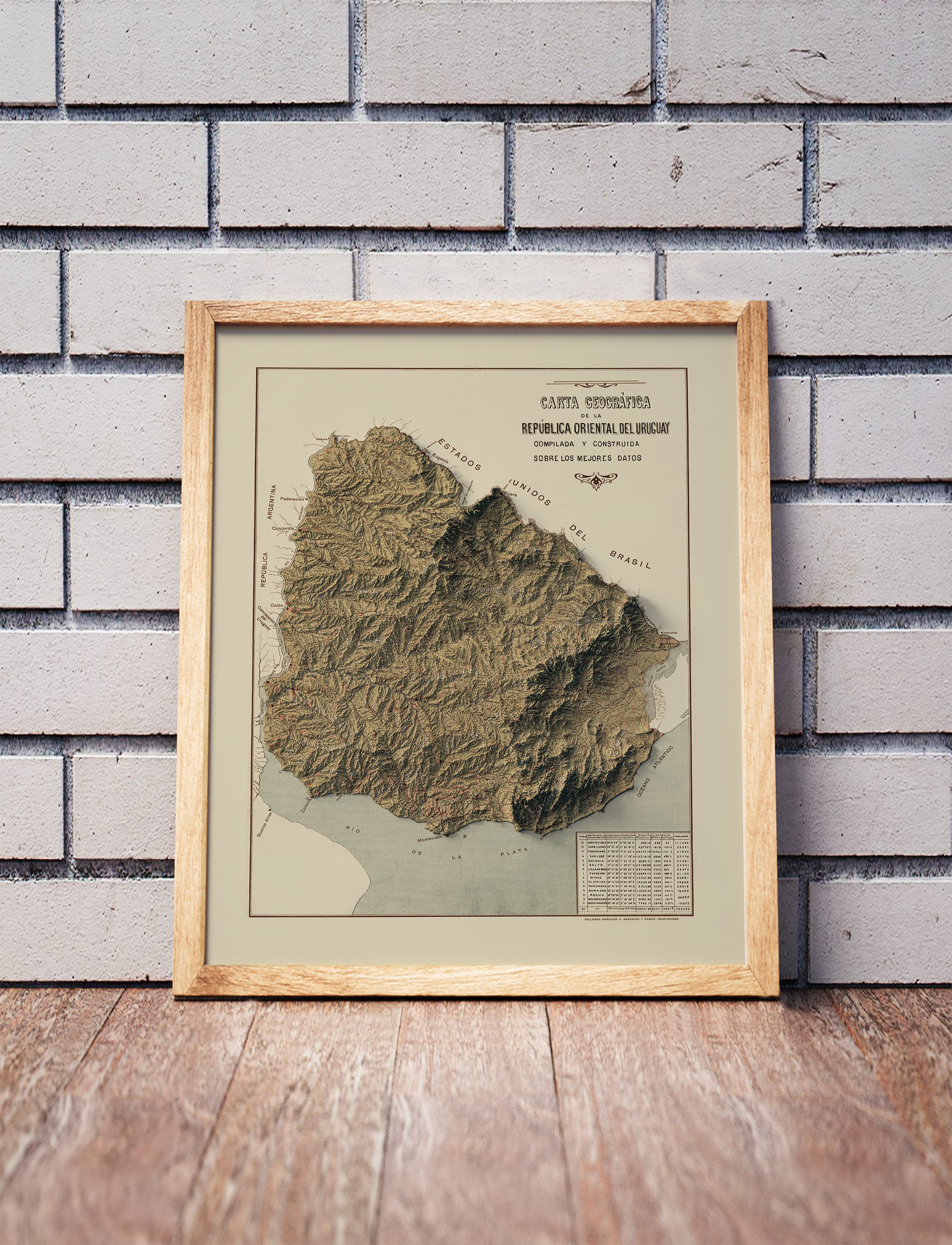 Vintage Uruguay shaded relief map in a wooden frame. Realistic terrain art print for home decor, displayed against a brick wall