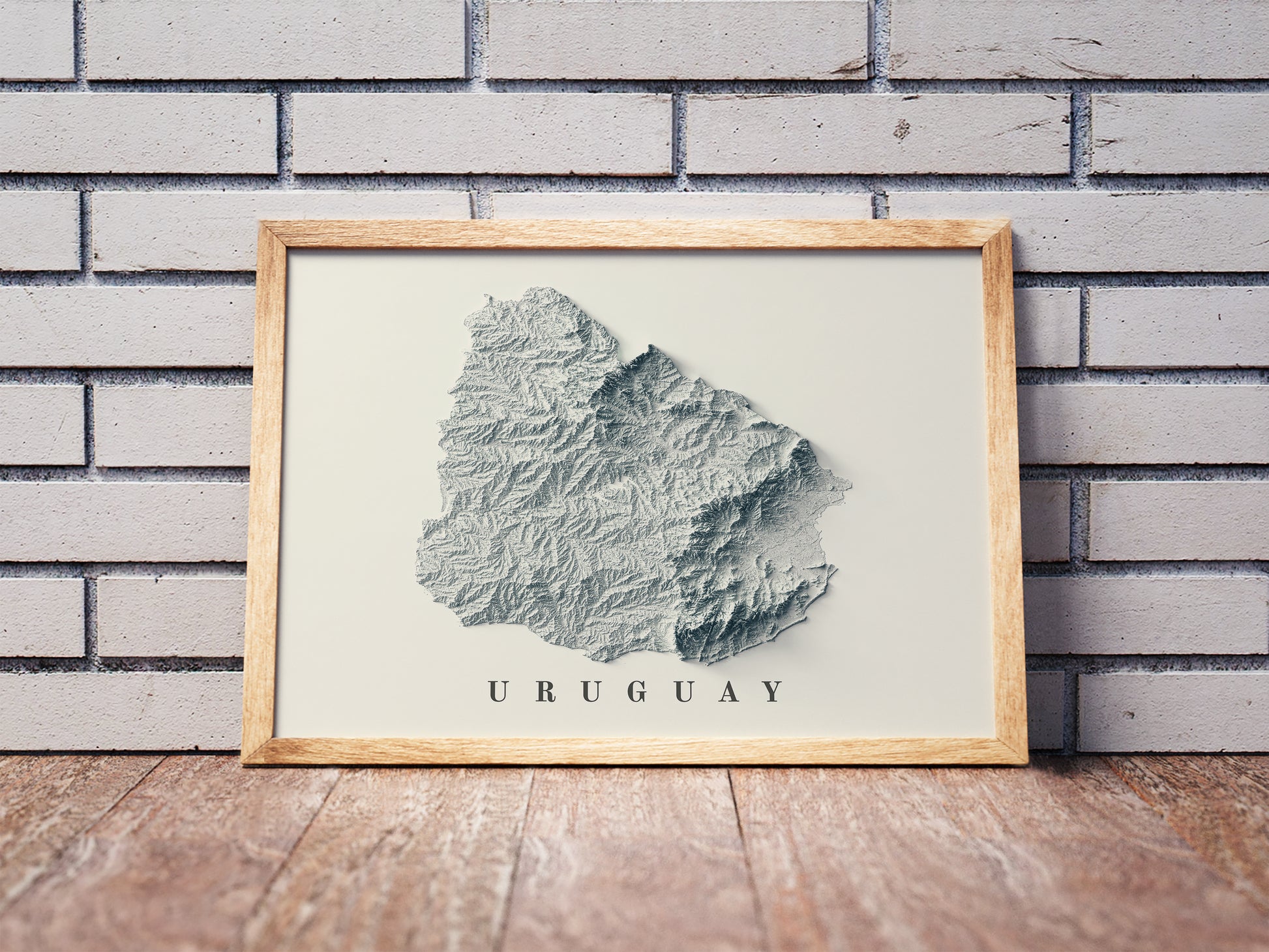 Uruguay shaded relief map in a wooden frame. Realistic terrain art print for home decor, displayed against a brick wall