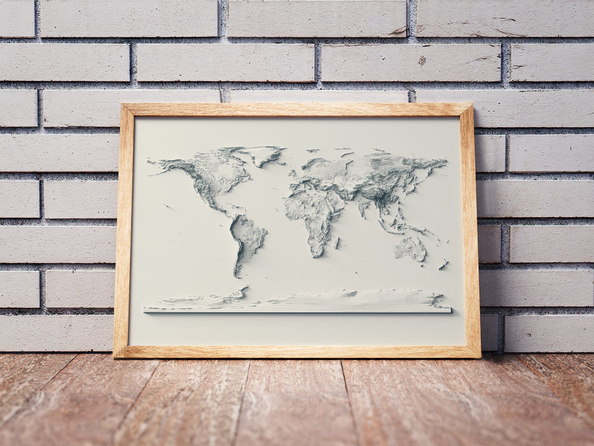World shaded relief map in a wooden frame. Realistic terrain art print for home decor, displayed against a brick wall