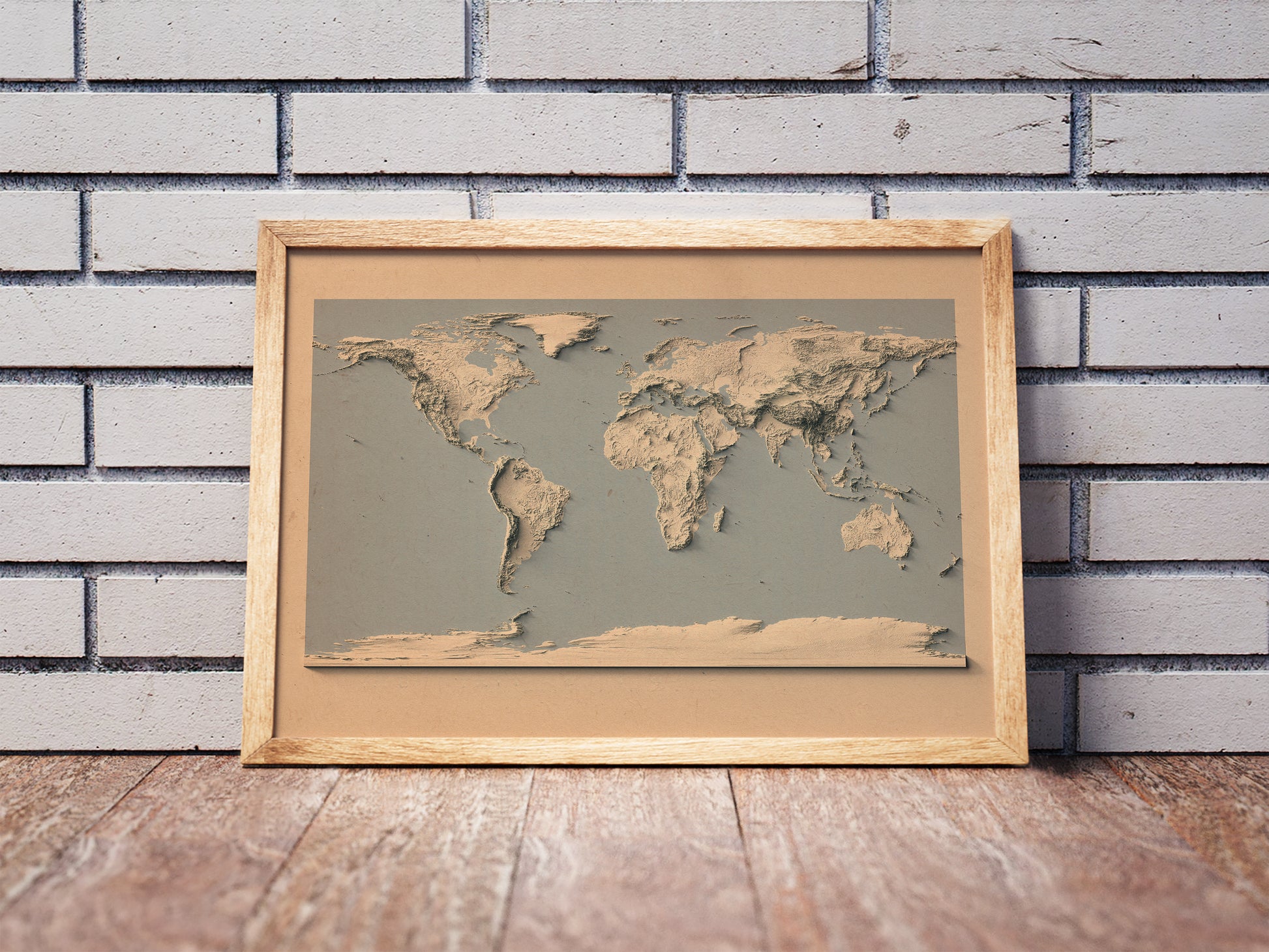 Vintage World shaded relief map and blue ocean in a wooden frame. Realistic terrain art print for home decor, displayed against a brick wall