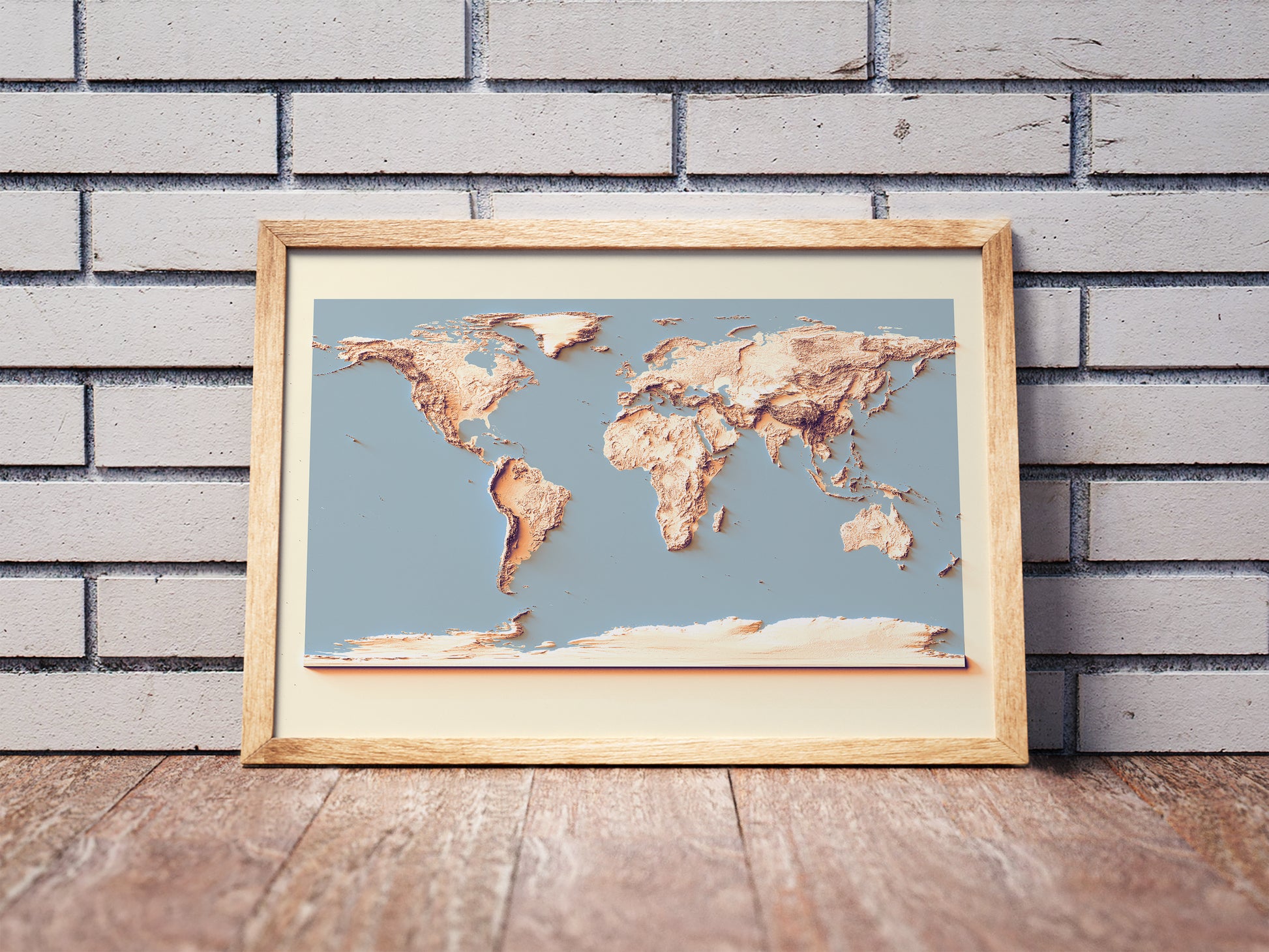 World shaded relief map with sunset tones in a wooden frame. Realistic terrain art print for home decor, displayed against a brick wall