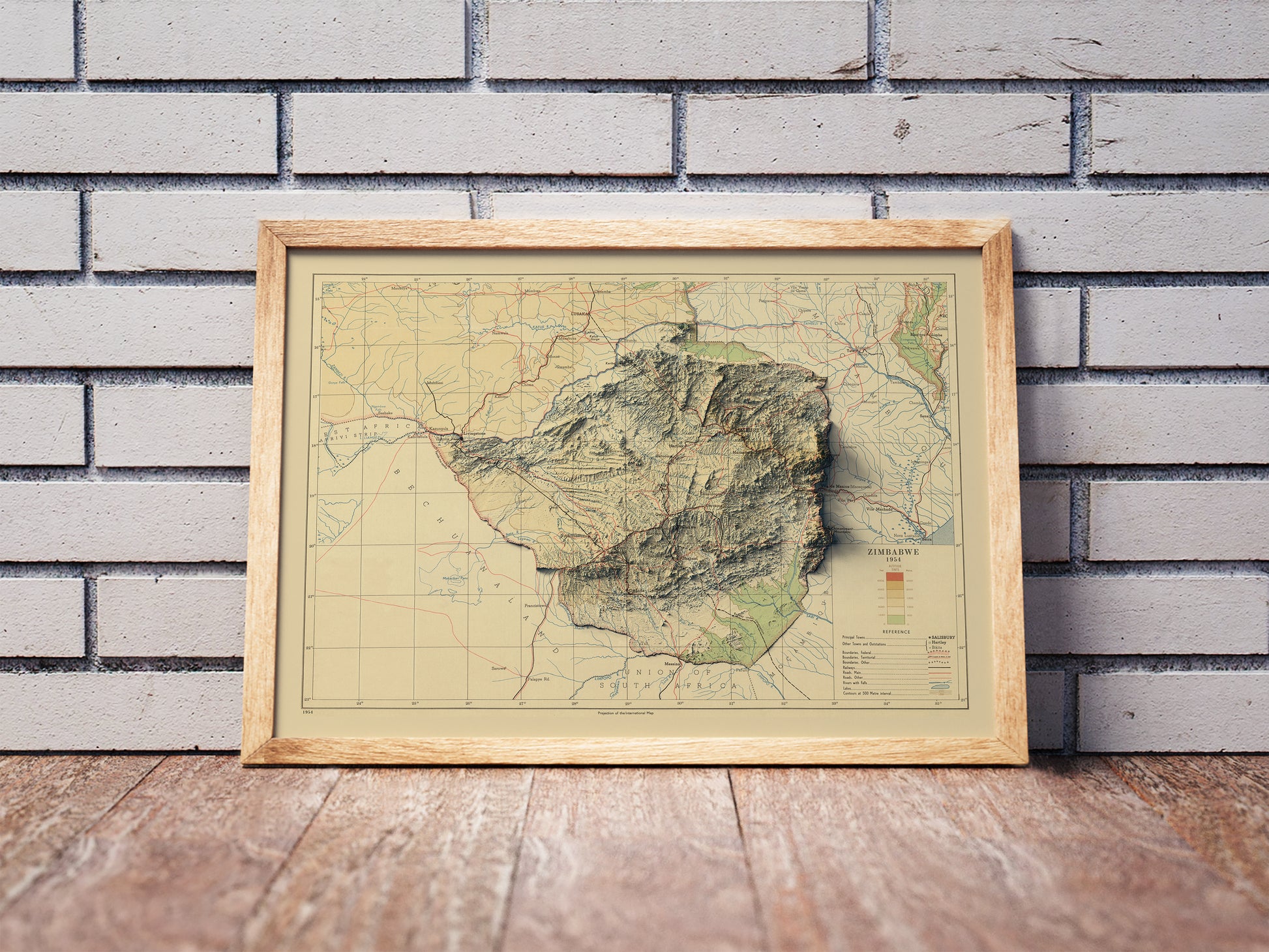 Vintage Zimbabwe shaded relief map in a wooden frame. Realistic terrain art print for home decor, displayed against a brick wall