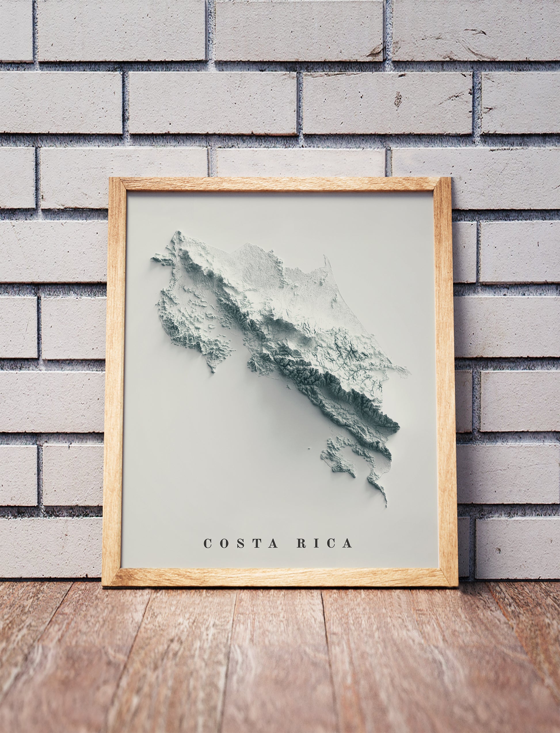 Costa Rica shaded relief map in a wooden frame. Realistic terrain art print for home decor, displayed against a brick wall