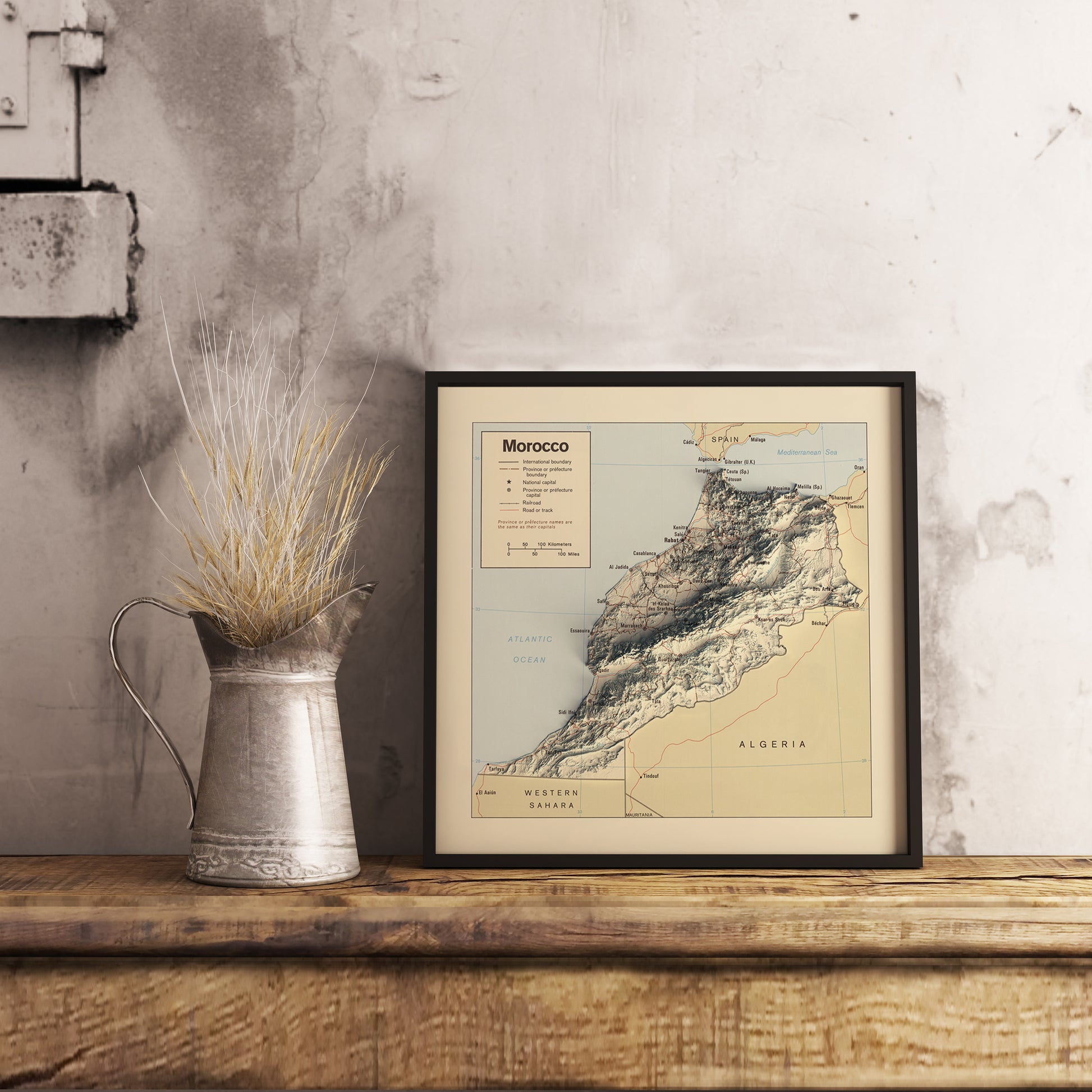 Vintage Morocco shaded relief map in black frame. Realistic terrain art print for home decor, displayed on rustic wooden table