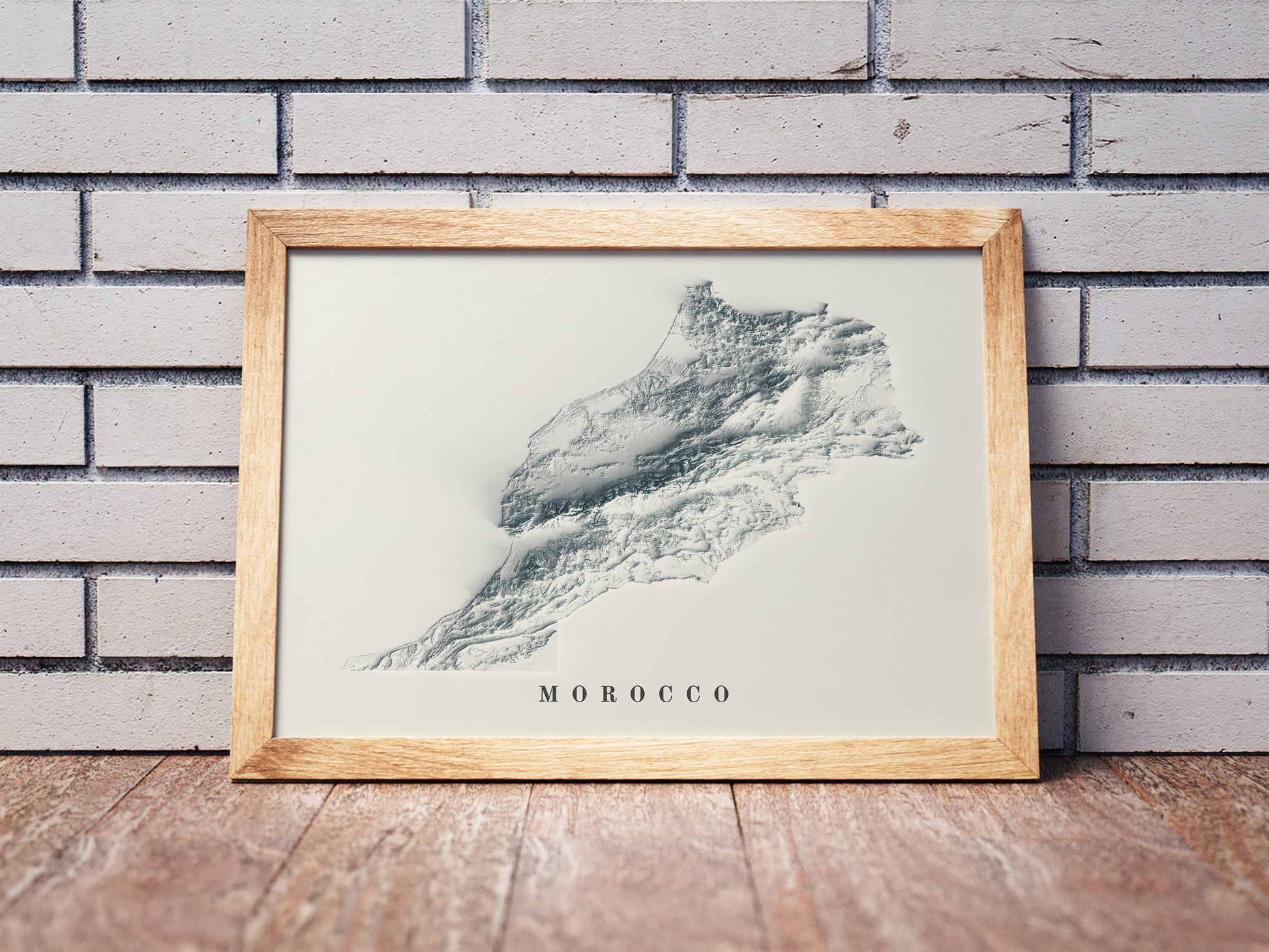 Vintage Morocco shaded relief map in a wooden frame. Realistic terrain art print for home decor, displayed against a brick wall