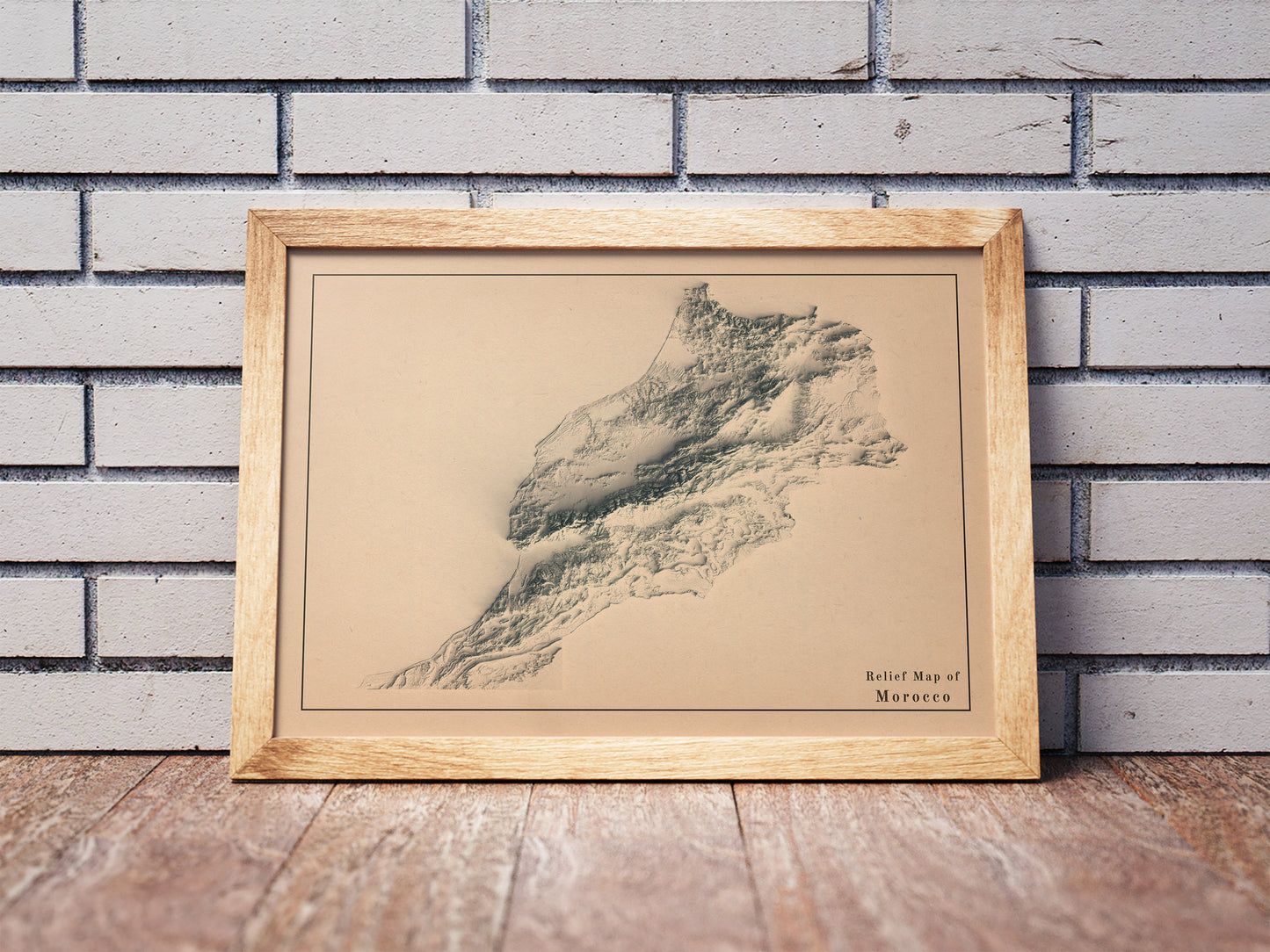 Vintage Morocco shaded relief map in a wooden frame. Realistic terrain art print for home decor, displayed against a brick wall