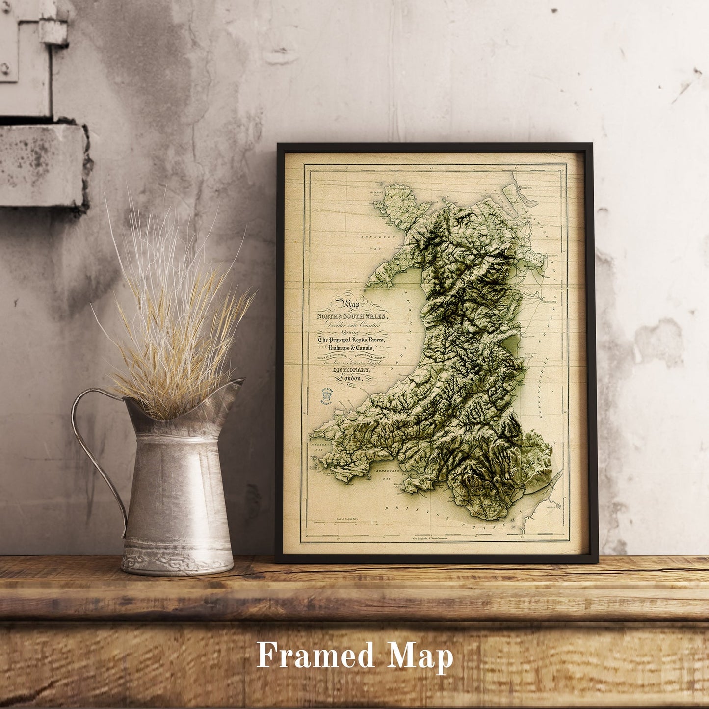 Vintage Wales shaded relief map in black frame. Realistic terrain art print for home decor, displayed on rustic wooden table
