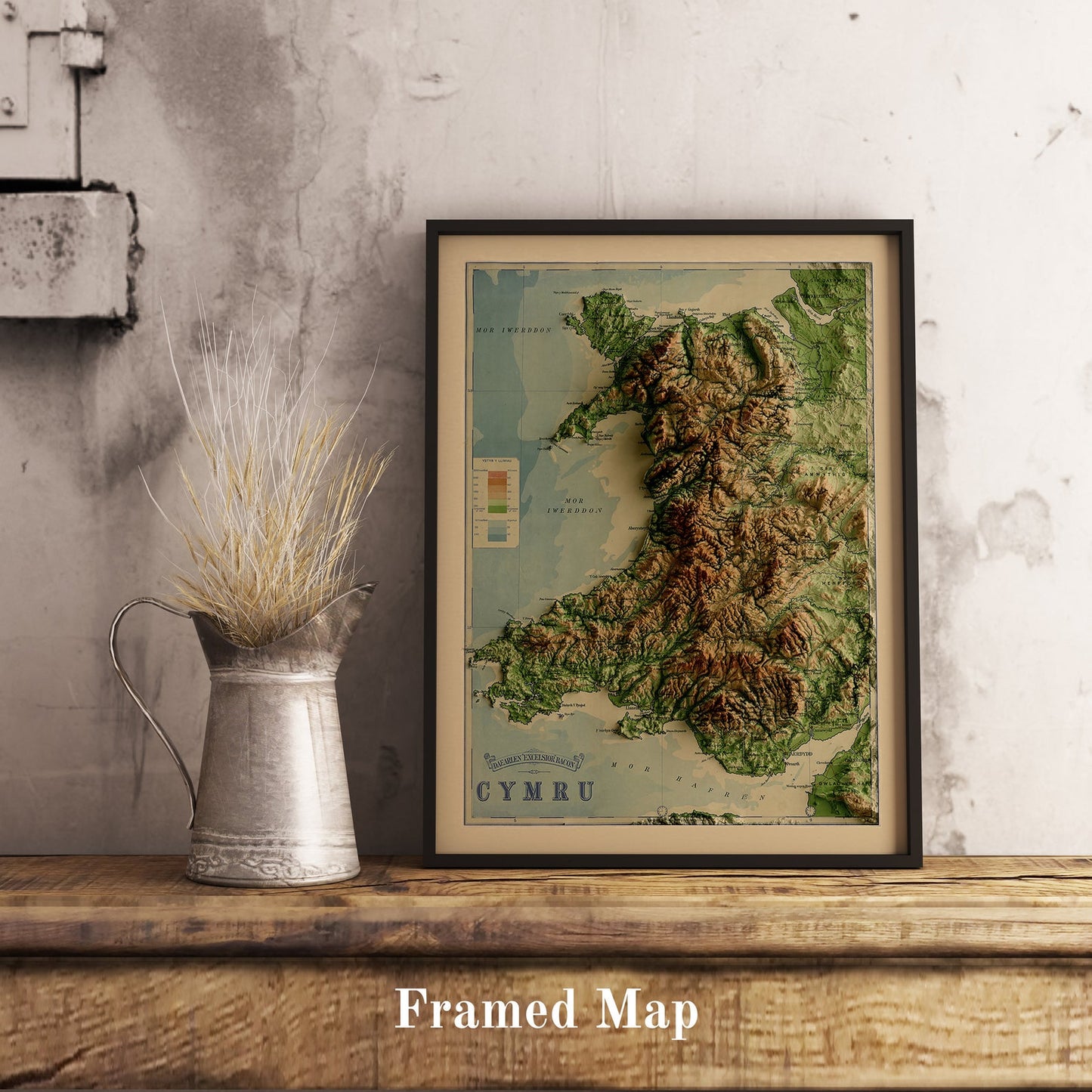 Vintage Wales shaded relief map in black frame. Realistic terrain art print for home decor, displayed on rustic wooden table