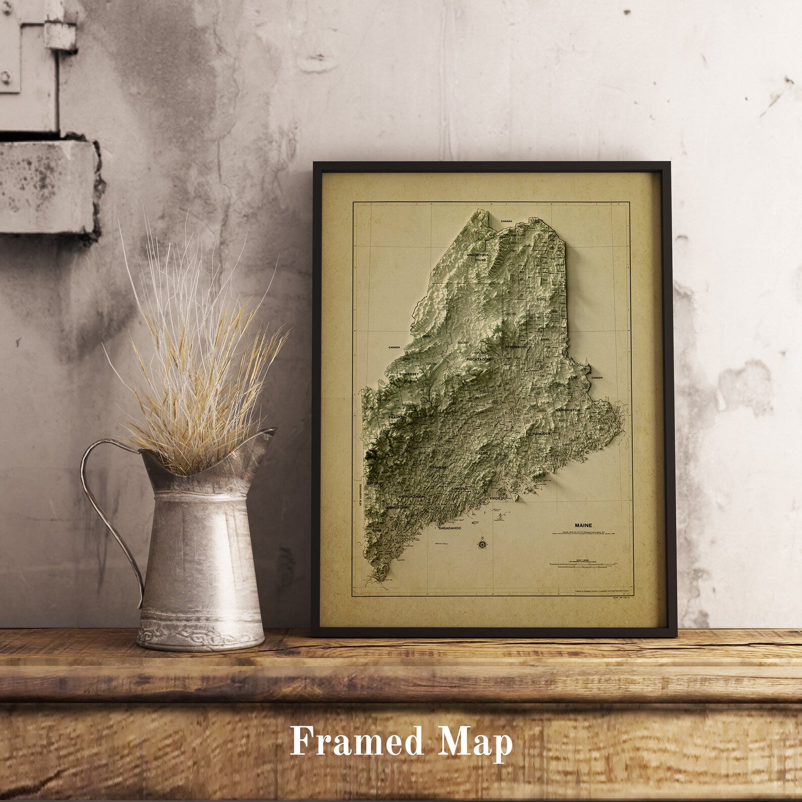 Vintage Maine shaded relief map in black frame. Realistic terrain art print for home decor, displayed on rustic wooden table