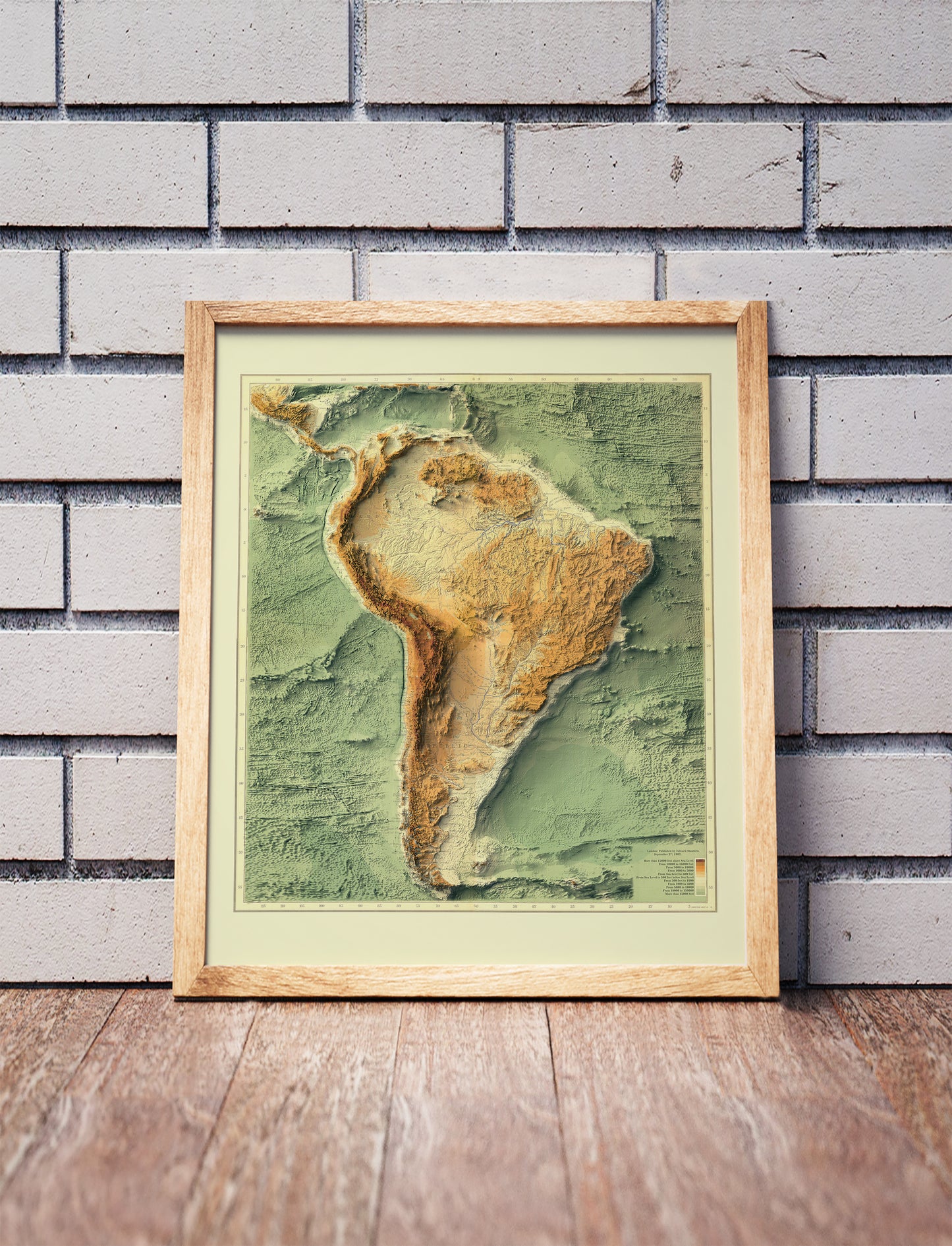 Vintage South America Bathymetrical shaded relief map in a wooden frame. Realistic terrain art print for home decor, displayed against a brick wall