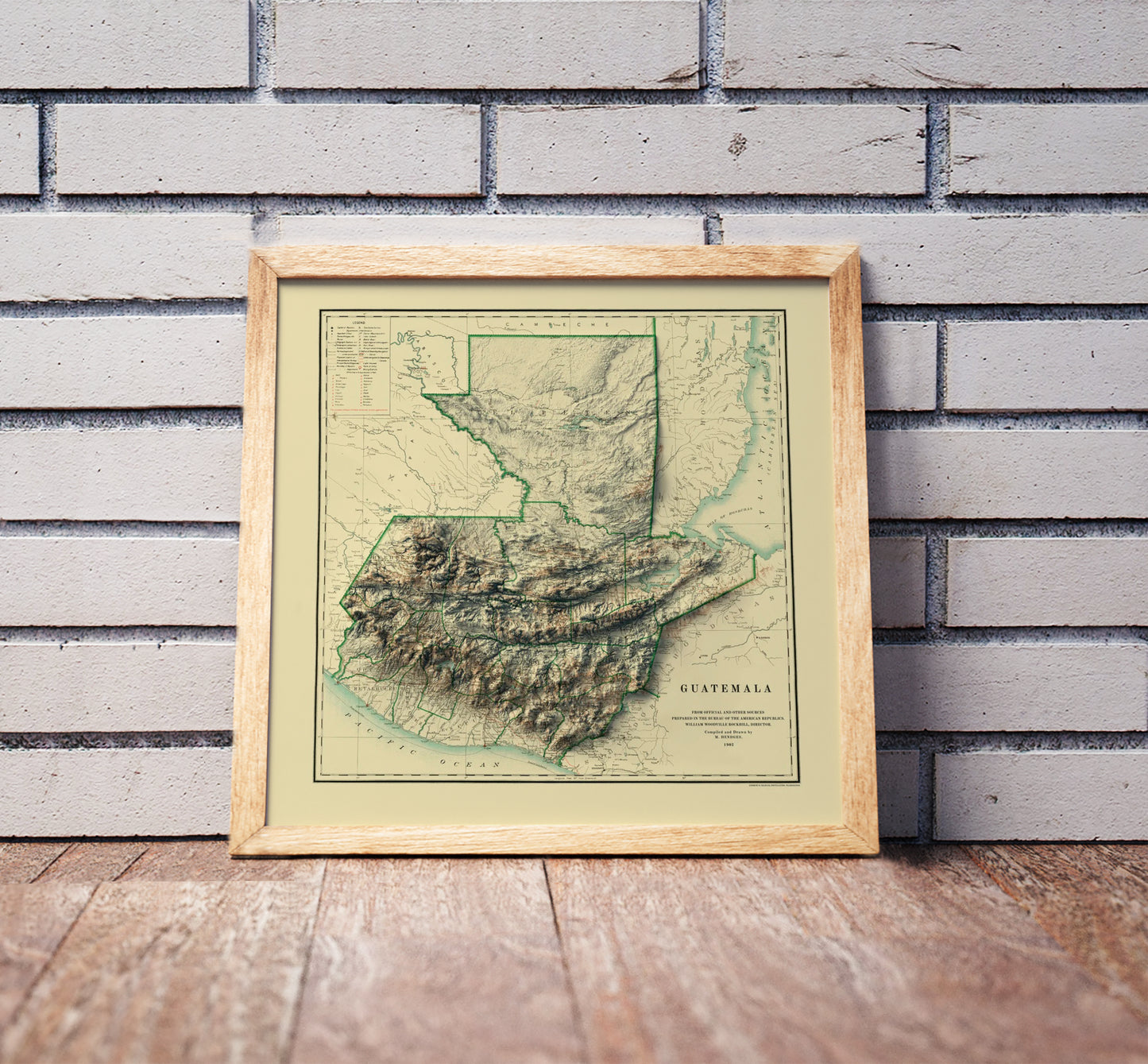 Vintage Guatemala shaded relief map in a wooden frame. Realistic terrain art print for home decor, displayed against a brick wall