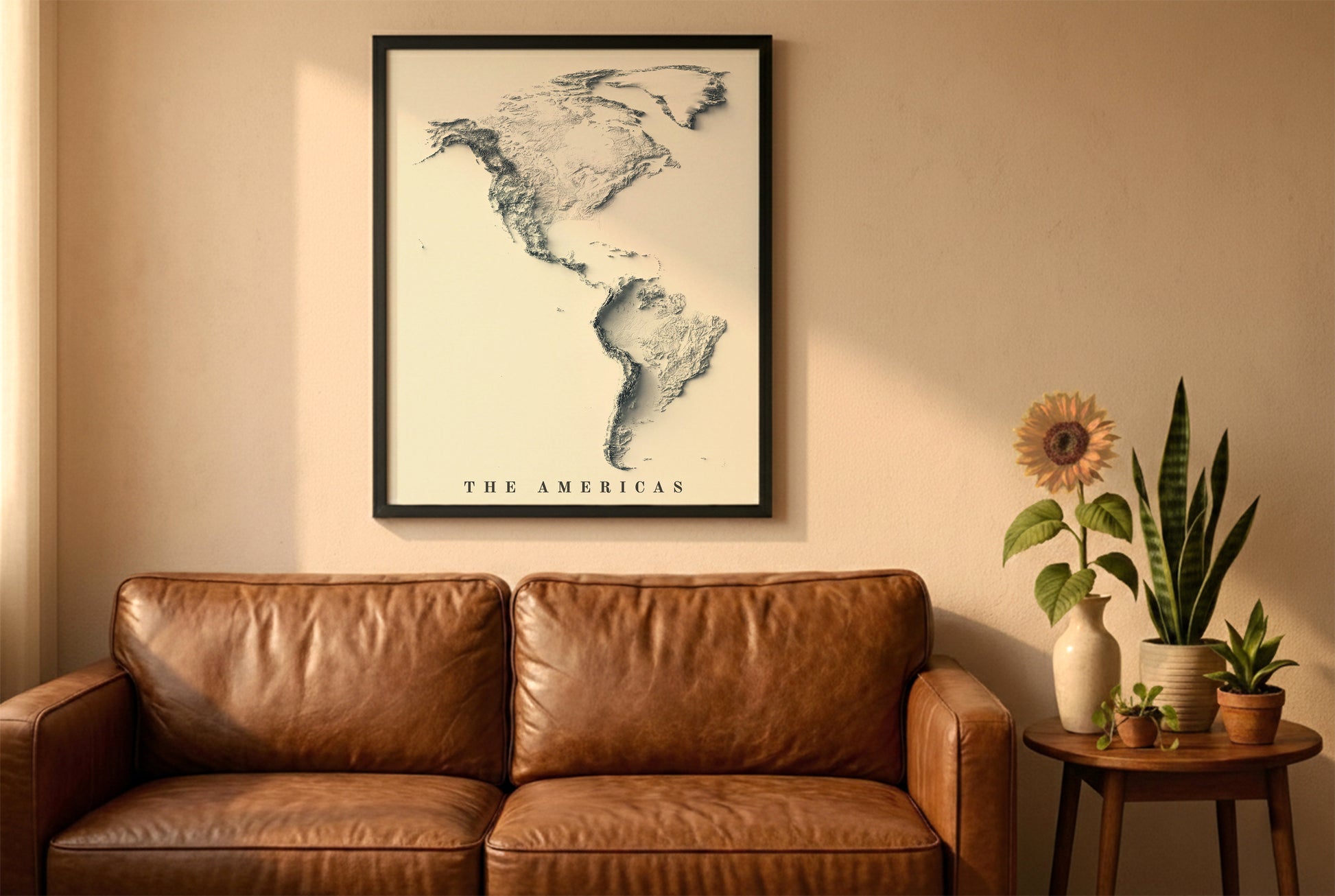 The Americas relief map in a black frame above a brown leather sofa. Boho living room with warm sunlight, sunflower, and indoor plants on a wooden side table