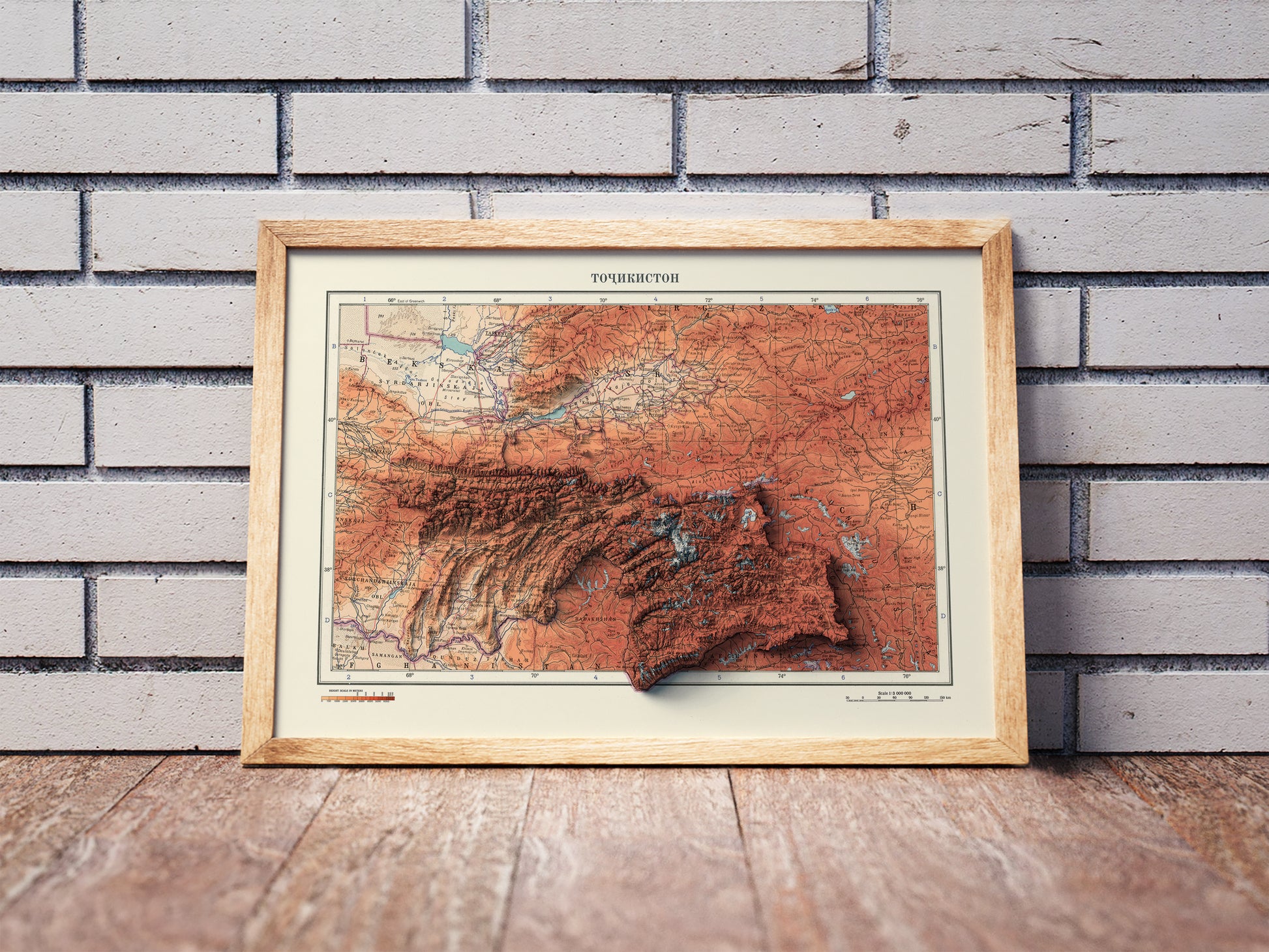 Vintage Tajikistan shaded relief map in a wooden frame. Realistic terrain art print for home decor, displayed against a brick wall