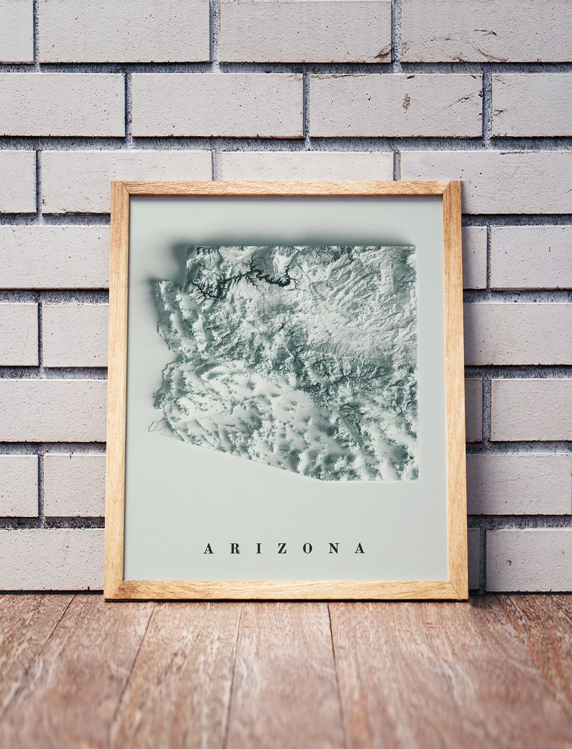 Arizona shaded relief map in a wooden frame. Realistic terrain art print for home decor, displayed against a brick wall