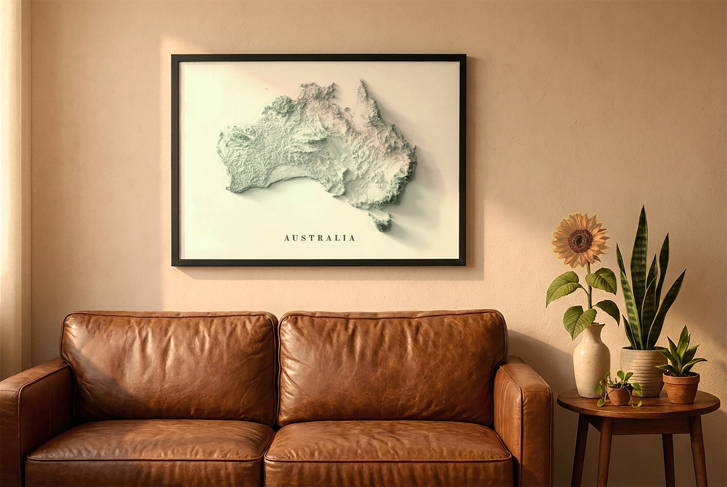 Australia relief map in a black frame above a brown leather sofa. Boho living room with warm sunlight, sunflower, and indoor plants on a wooden side table