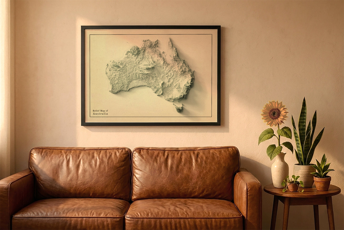 Australia relief map in a black frame above a brown leather sofa. Boho living room with warm sunlight, sunflower, and indoor plants on a wooden side table