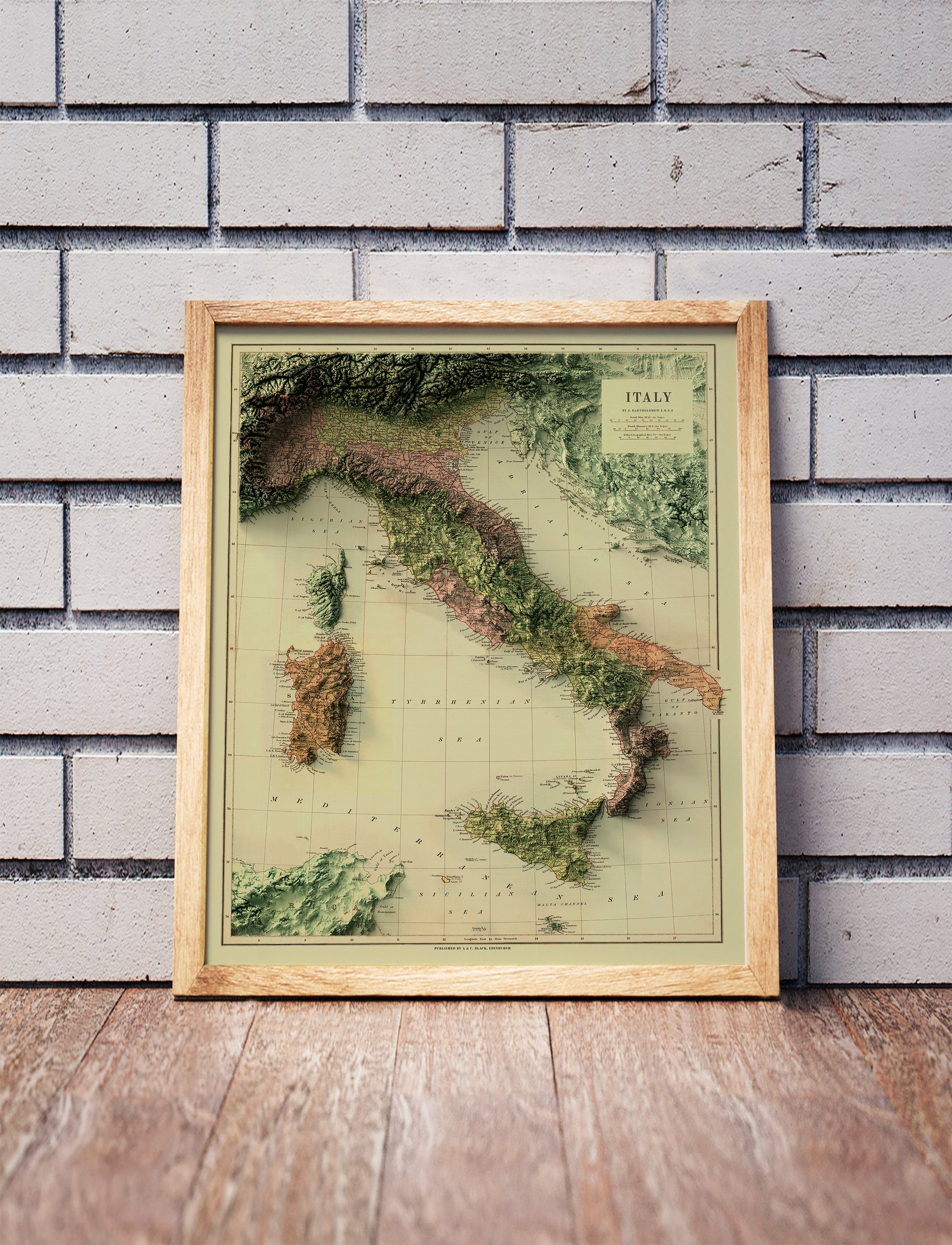 Vintage Italy shaded relief map in a wooden frame. Realistic terrain art print for home decor, displayed against a brick wall