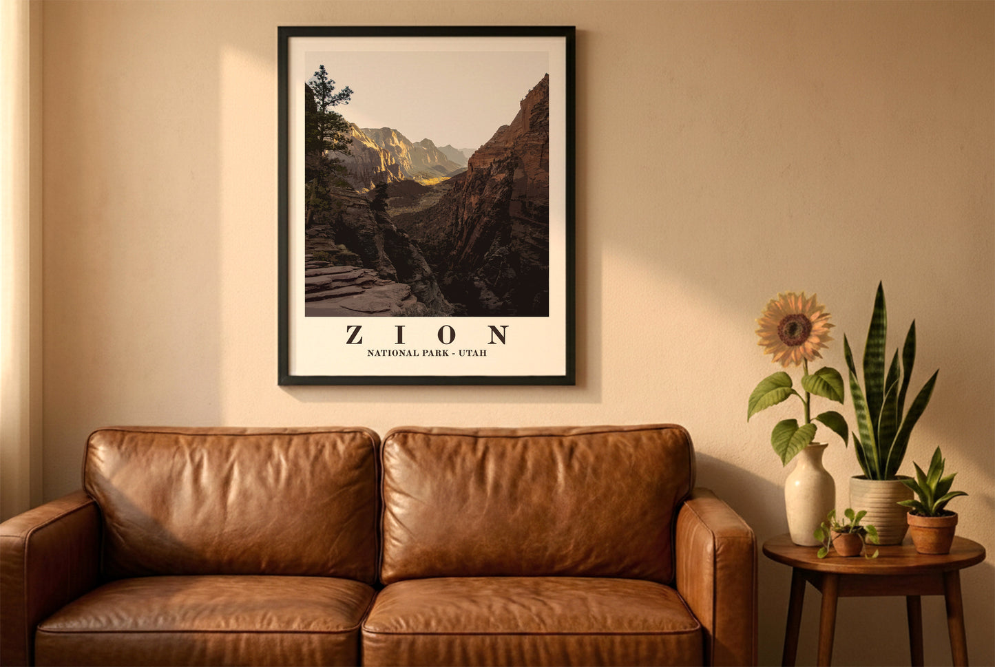 Zion National Park poster in a black frame above a brown leather sofa. Boho living room with warm sunlight, sunflower, and indoor plants on a wooden side table