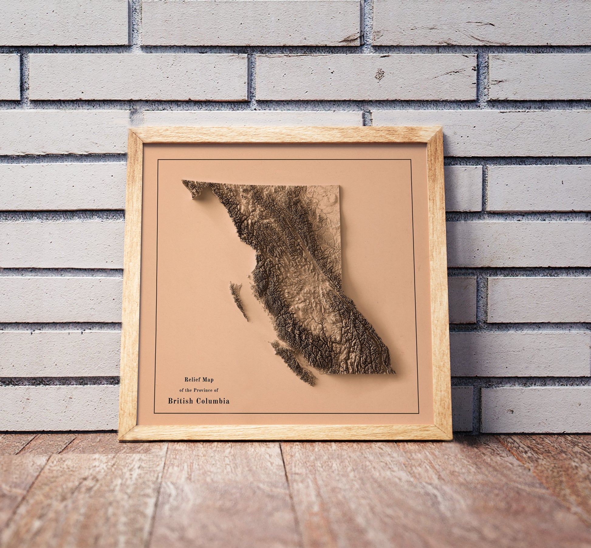 Vintage British Columbia, Canada, shaded relief map in a wooden frame. Realistic terrain art print for home decor, displayed against a brick wall
