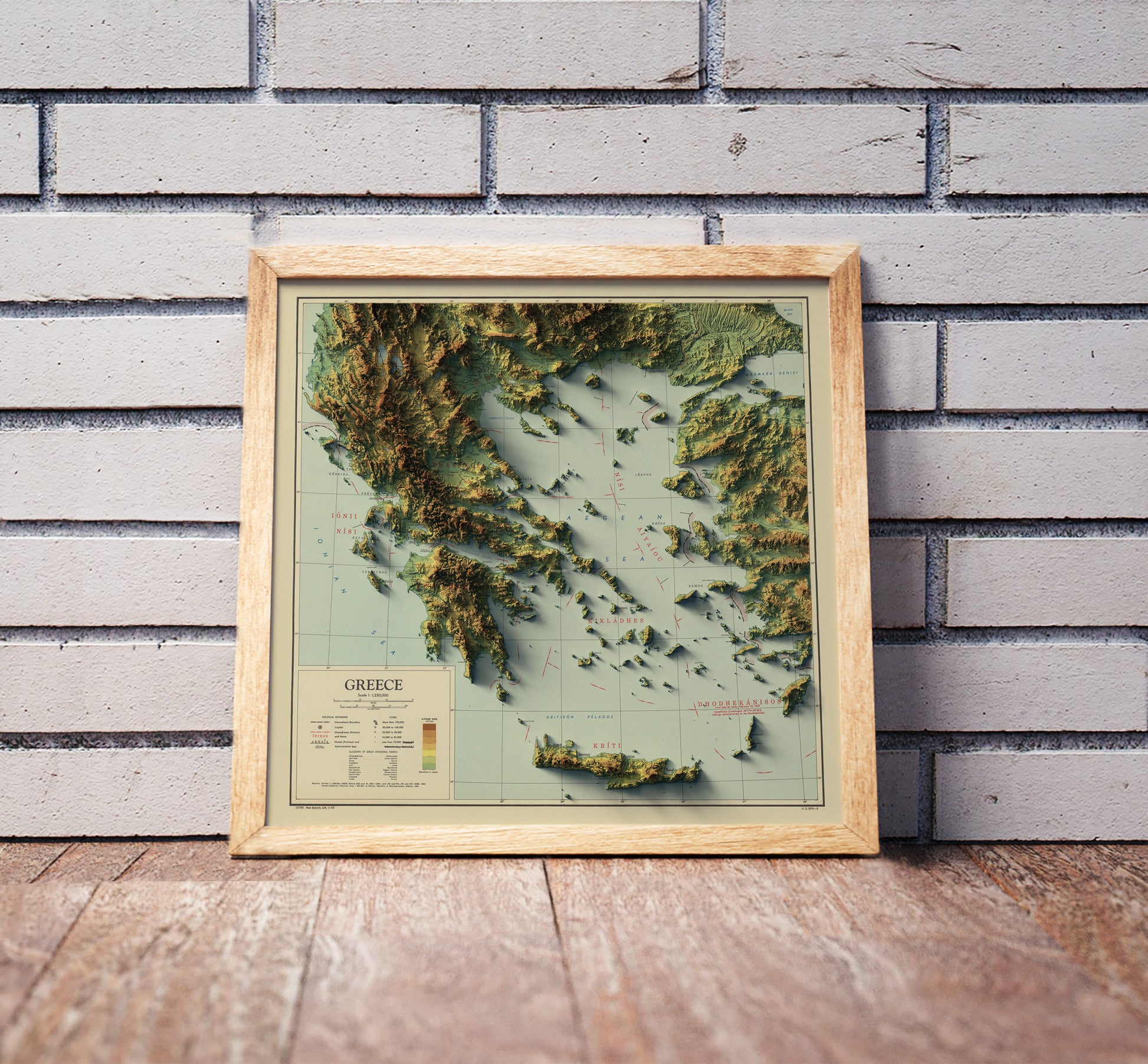 Vintage Greece shaded relief map in a wooden frame. Realistic terrain art print for home decor, displayed against a brick wall