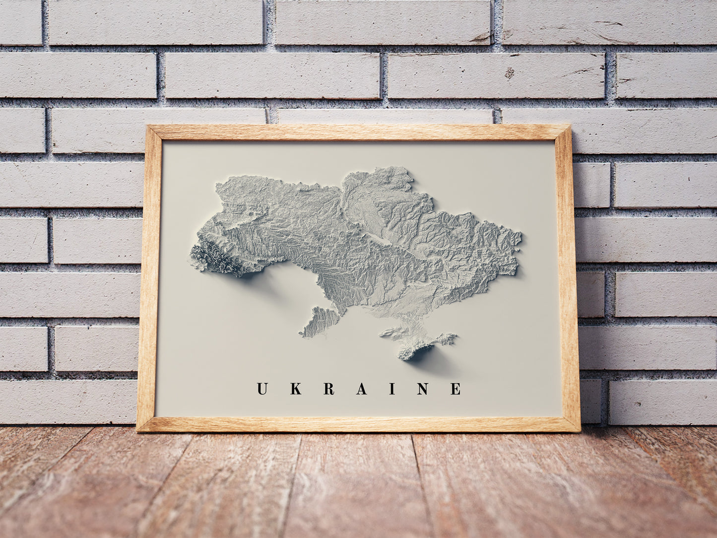 Ukraine shaded relief map in a wooden frame. Realistic terrain art print for home decor, displayed against a brick wall
