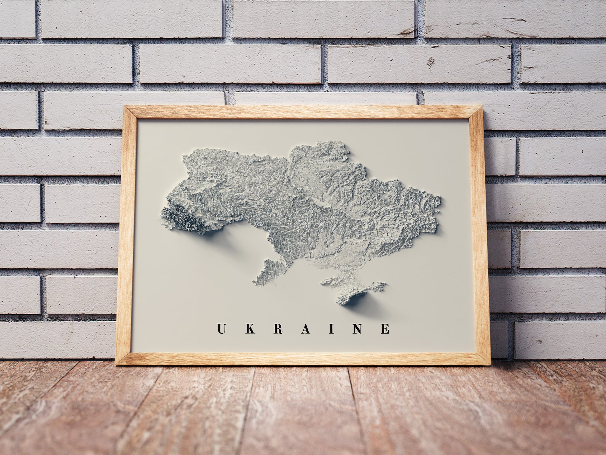 Ukraine shaded relief map in a wooden frame. Realistic terrain art print for home decor, displayed against a brick wall