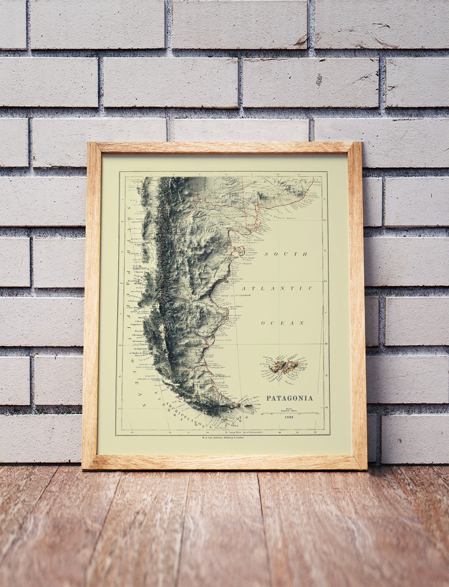 Vintage Patagonia shaded relief map in a wooden frame. Realistic terrain art print for home decor, displayed against a brick wall