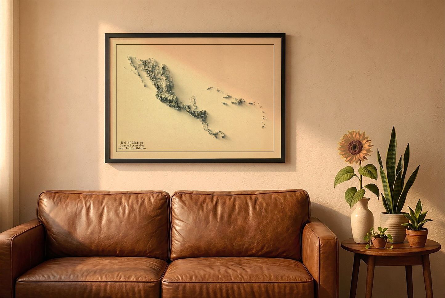 Central America and the Caribbean vintage relief map in a black frame above a brown leather sofa. Boho living room with warm sunlight, sunflower, and indoor plants on a wooden side table