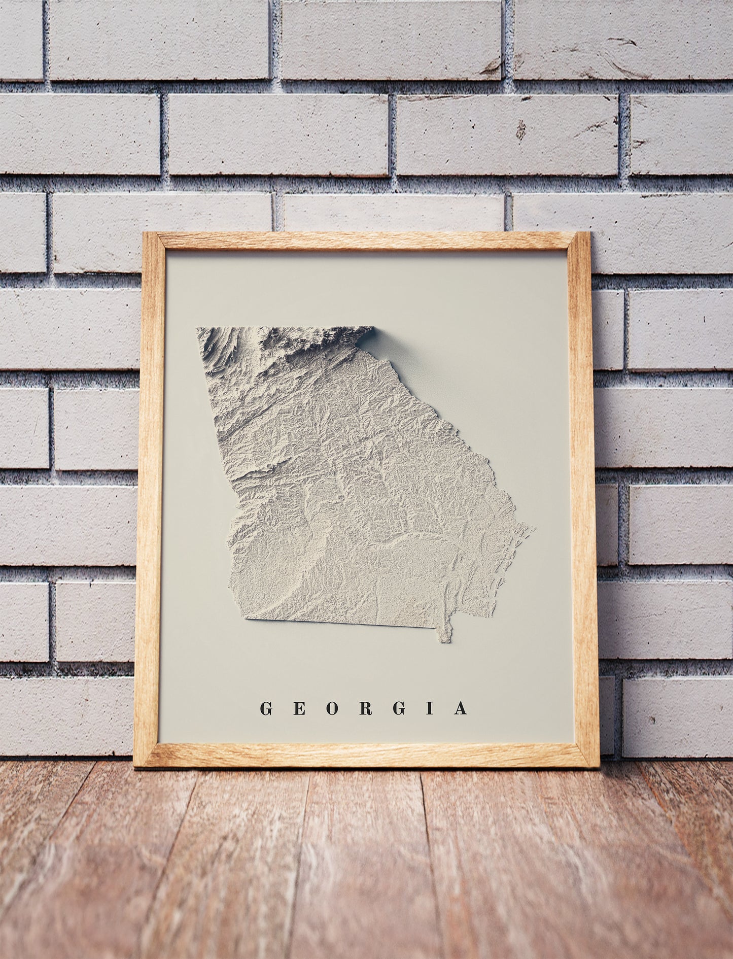Georgia shaded relief map in a wooden frame. Realistic terrain art print for home decor, displayed against a brick wall